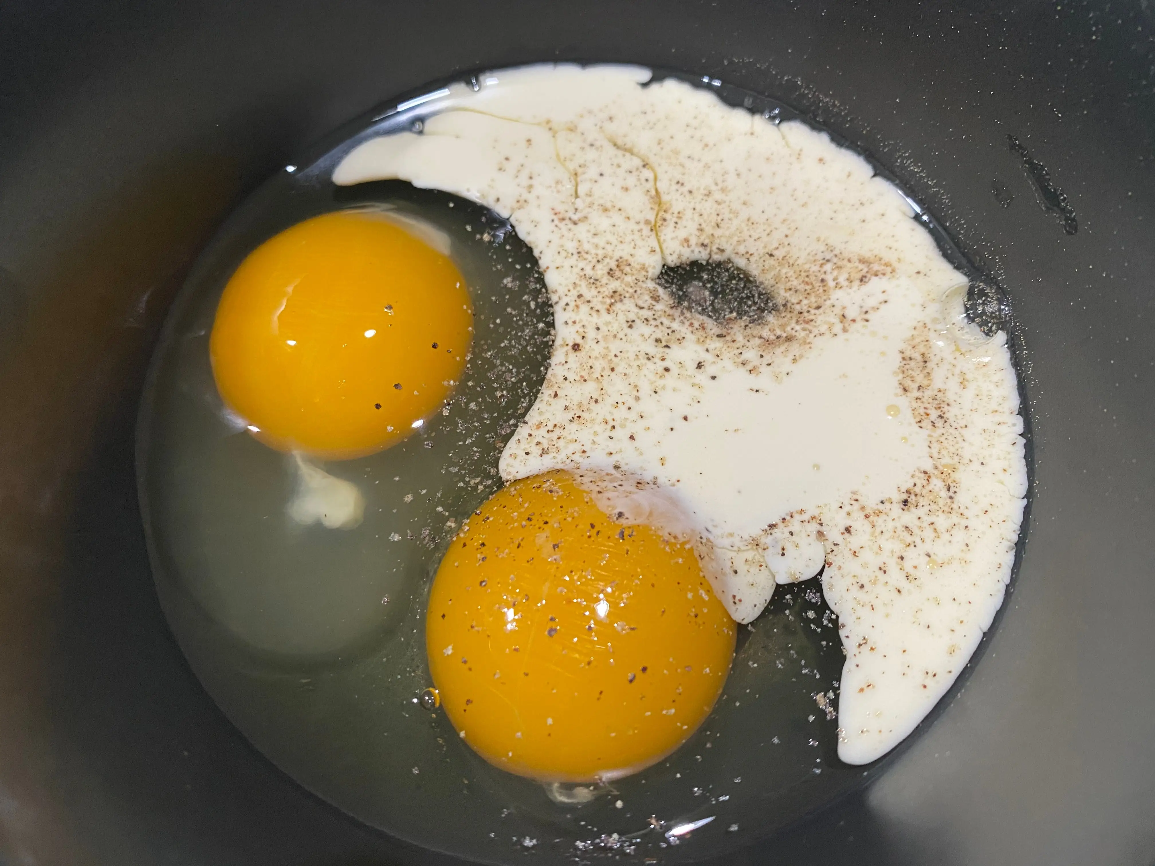 Two eggs in bowl with cream, salt, pepper