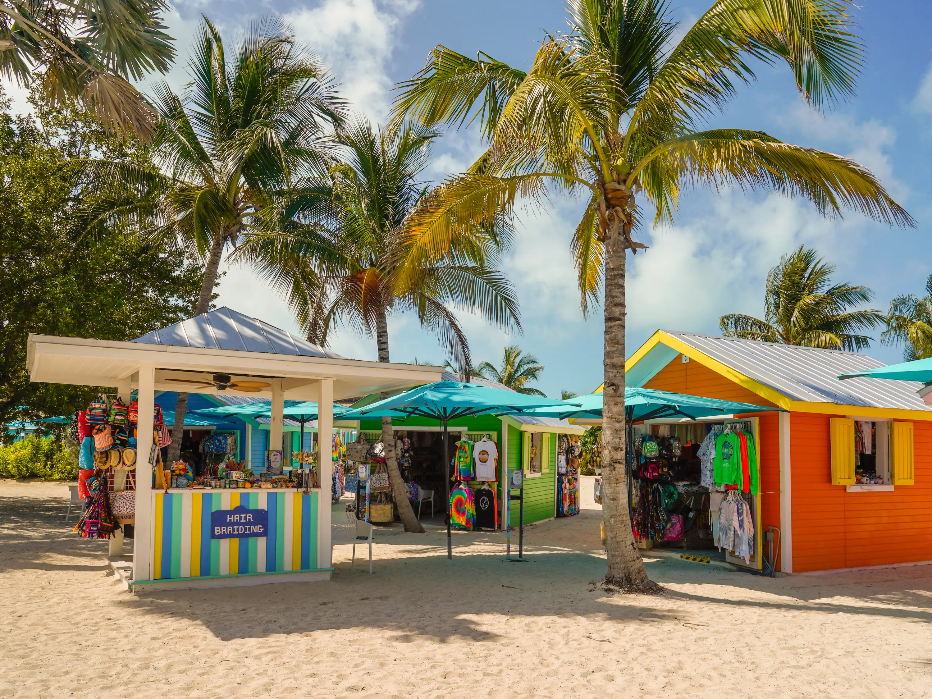 Shops in the sand between palm trees at CocoCay on a partly-cloudy day