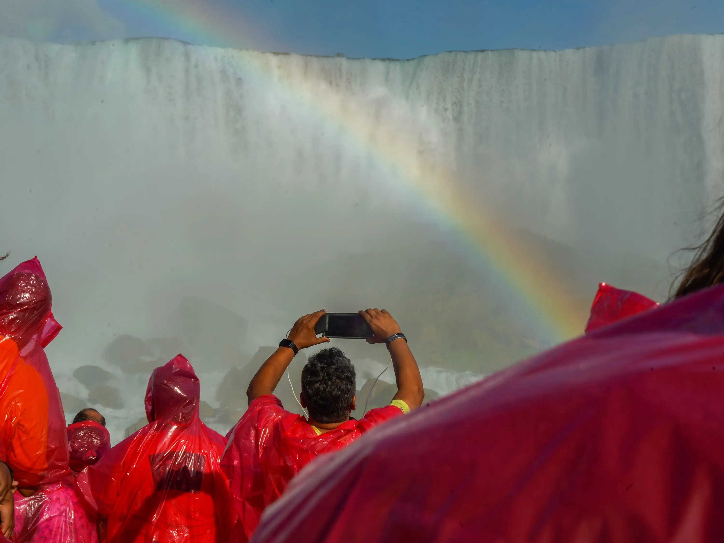 People on a boat take photos of a rainbow in front of Niagara Falls