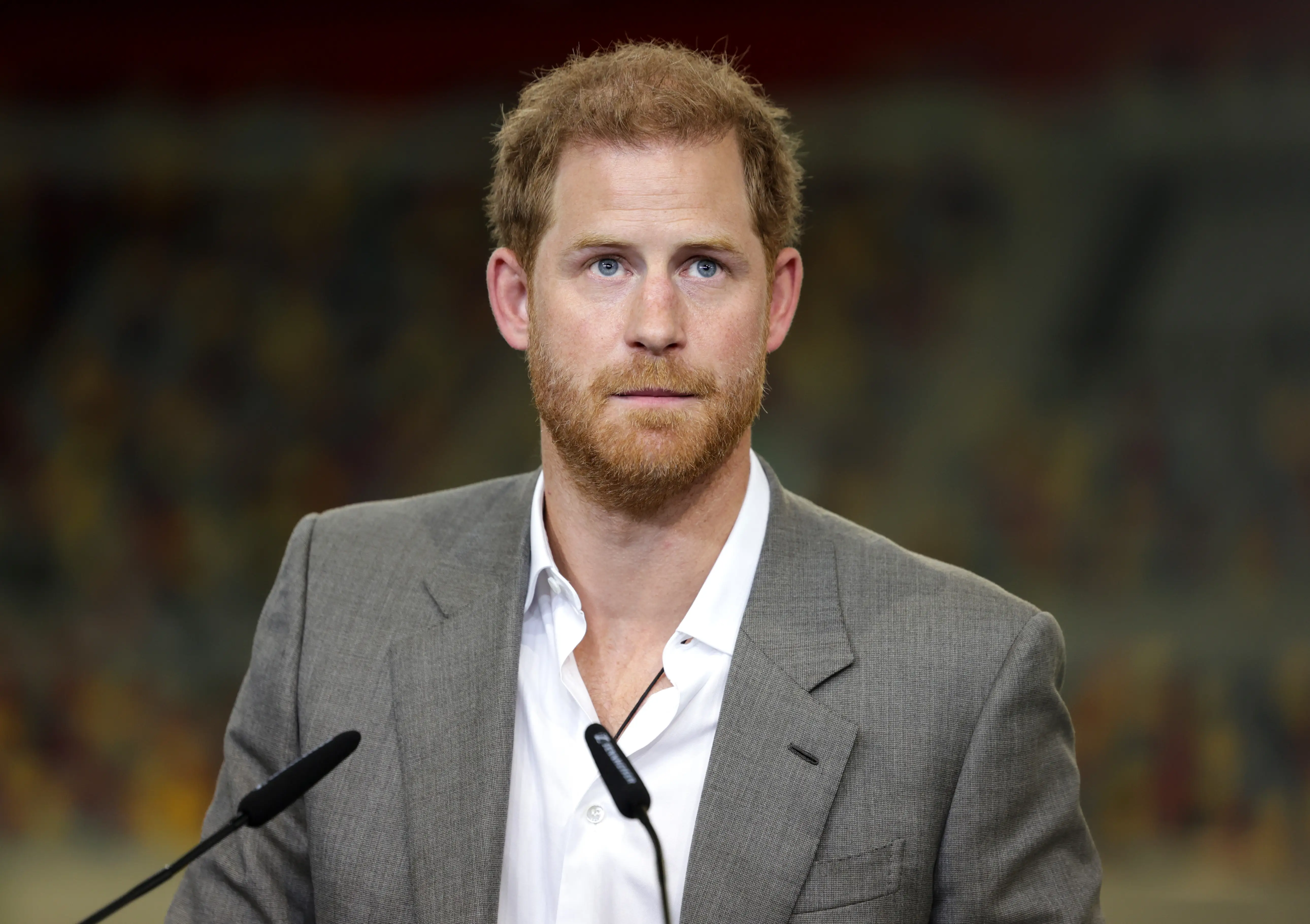Prince Harry speaks into a microphone in a gray jacket and a white shirt