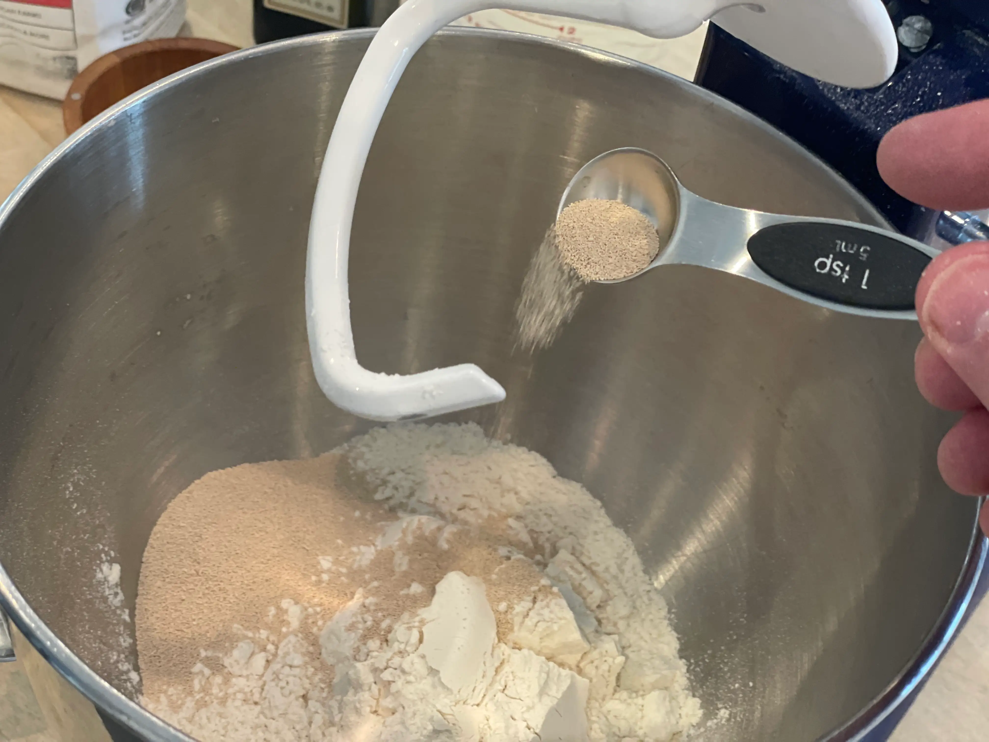 hand pouring a teaspoon of yeast into a bowl of flower