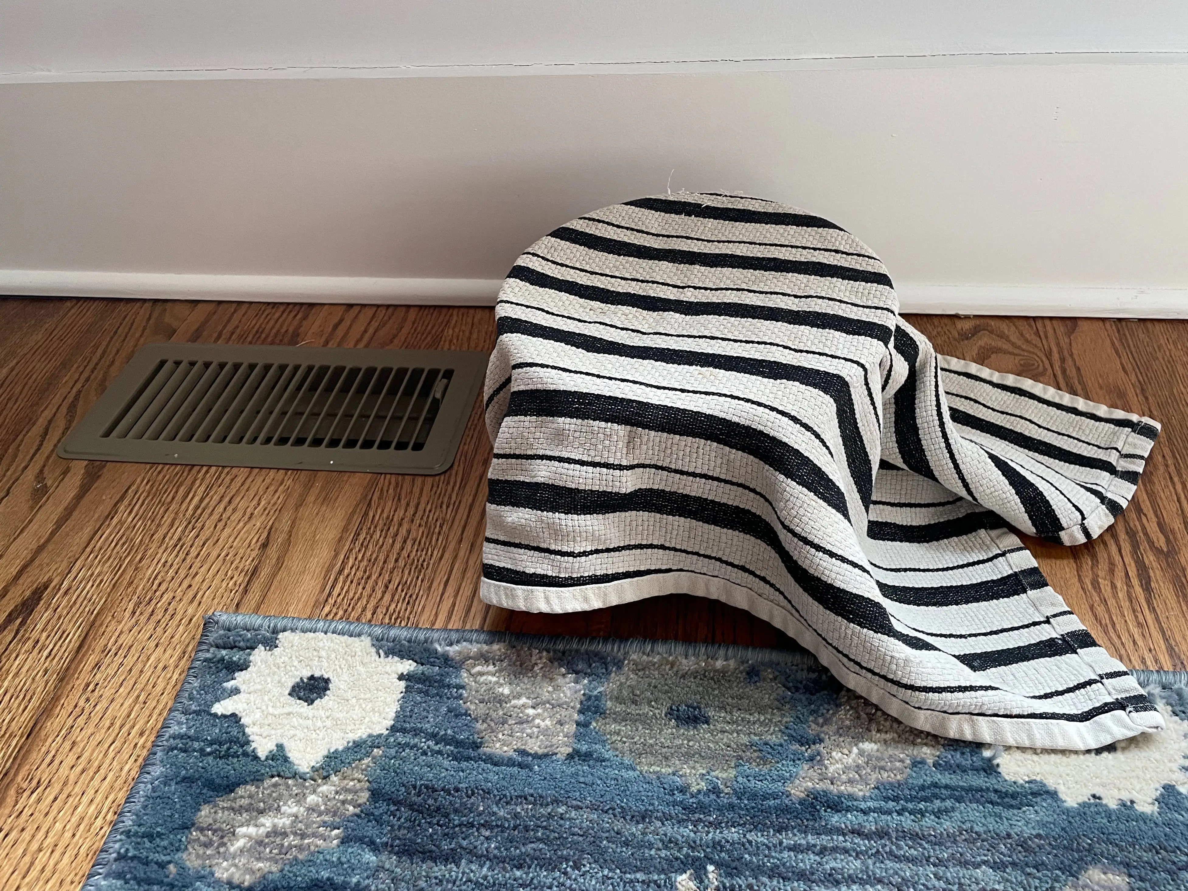 bowl covered with a kitchen towel sitting on the floor next to a heating vent