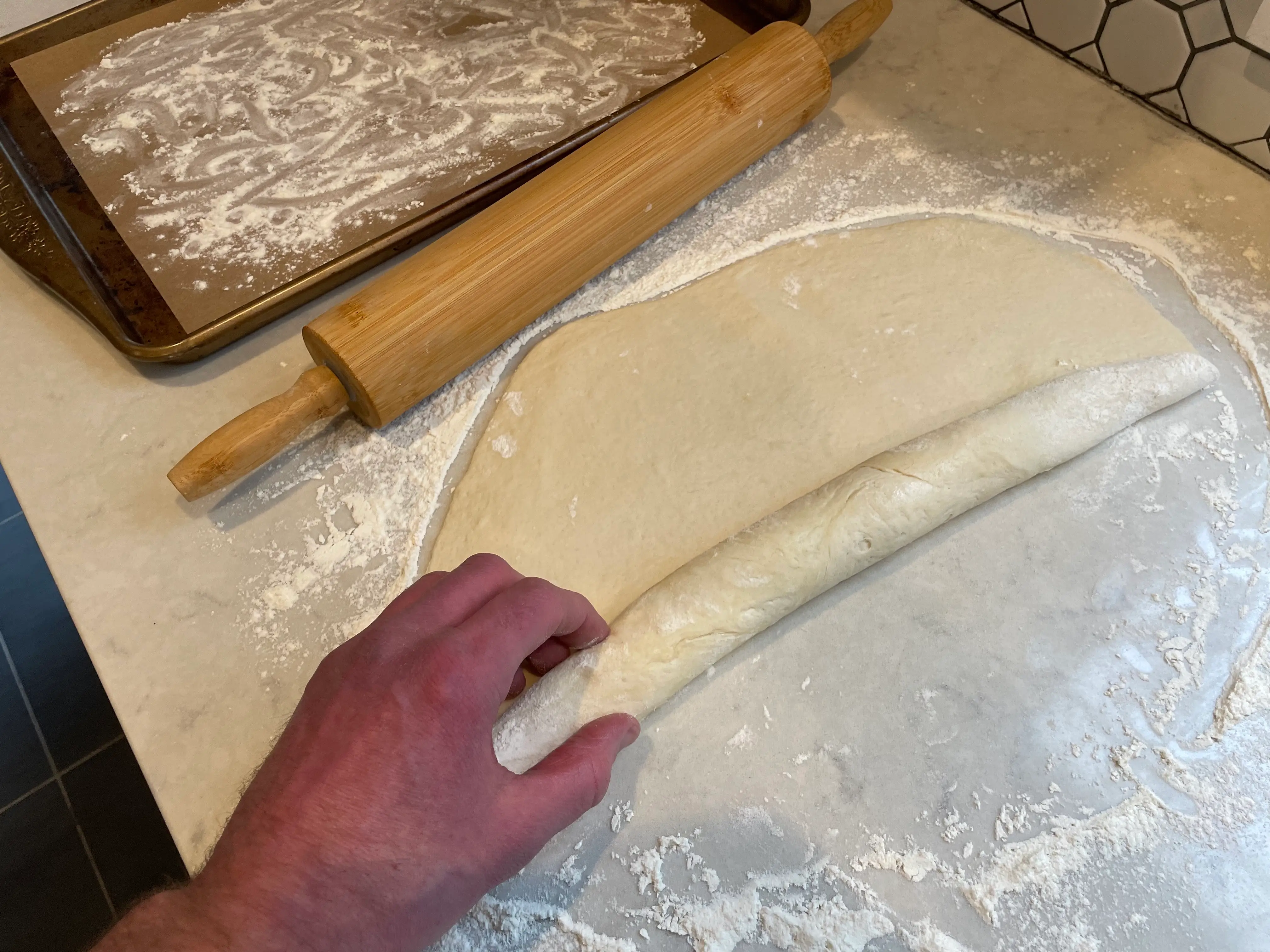 hand rolling up a sheet of flattened bread dough