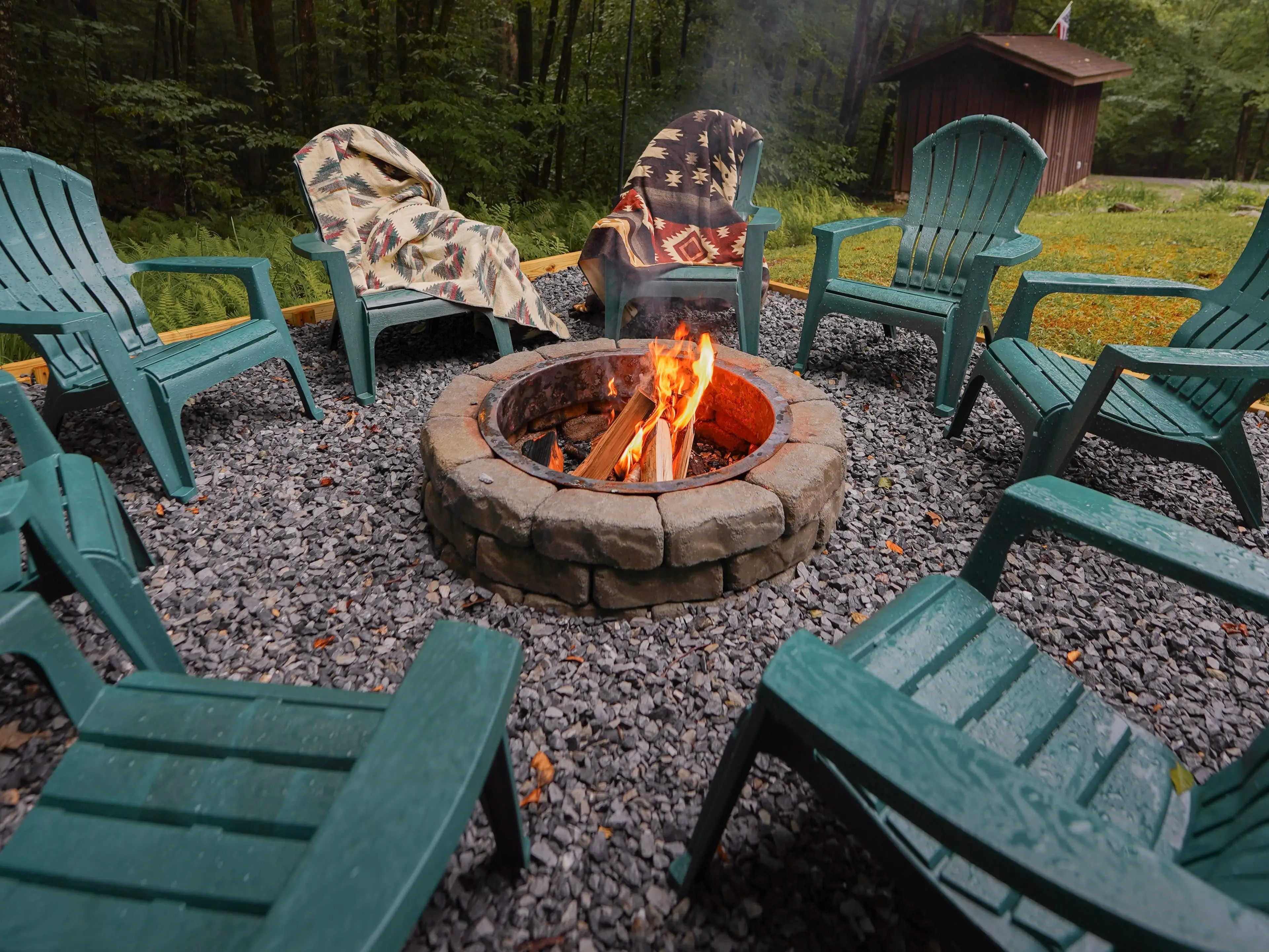Garden chairs circled round a fire pit, with two blankets on two of the chairs.