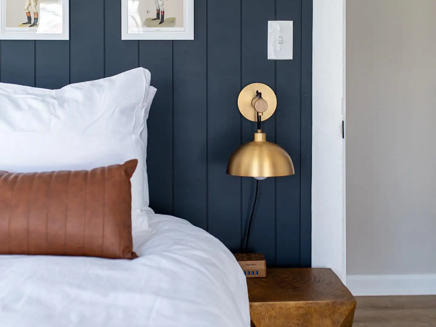 A bedside table with a brass lamp and artwork above it.