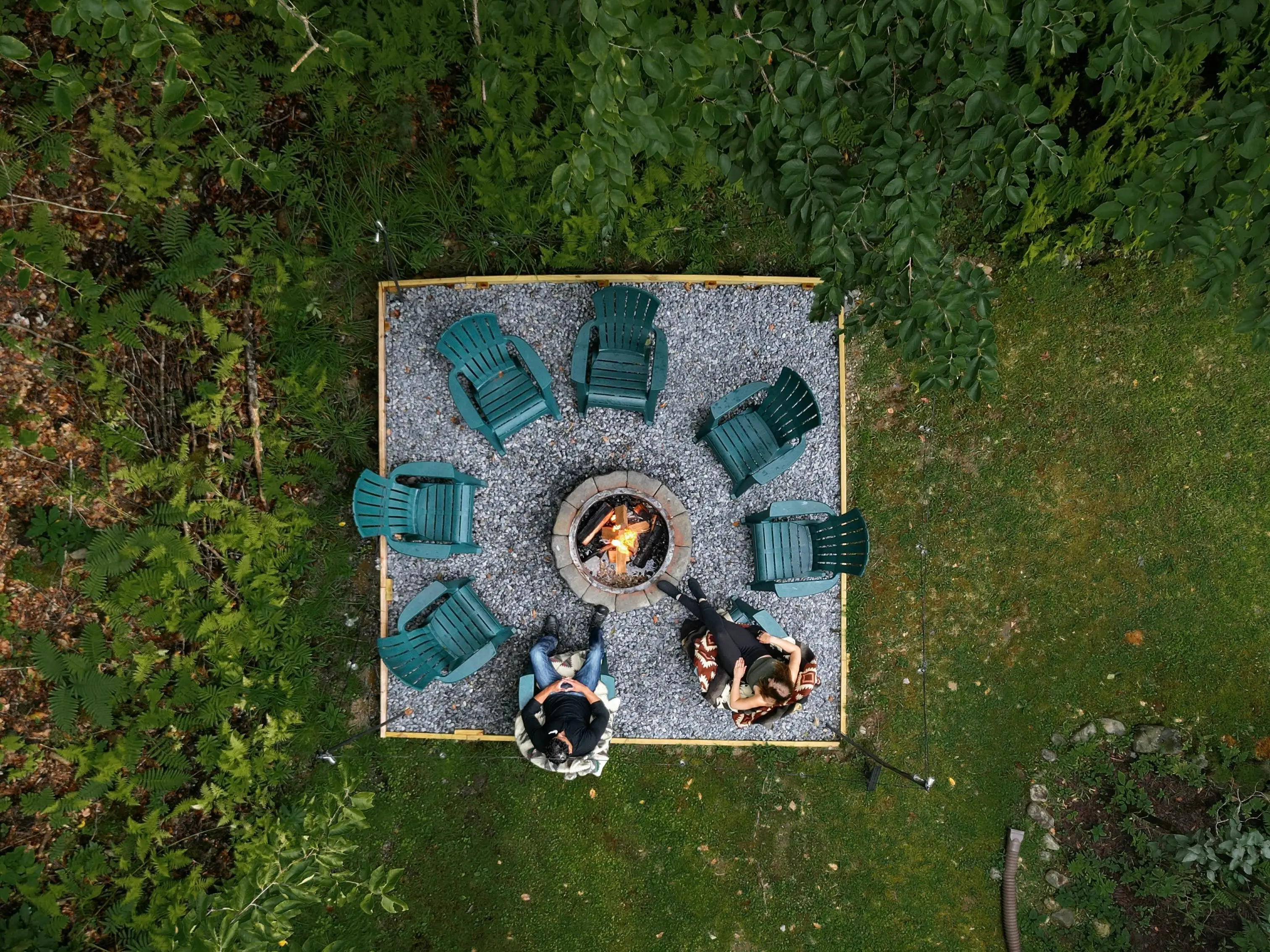An overhead view of two people sitting on garden chairs, which are arranged in a circle around a firepit.