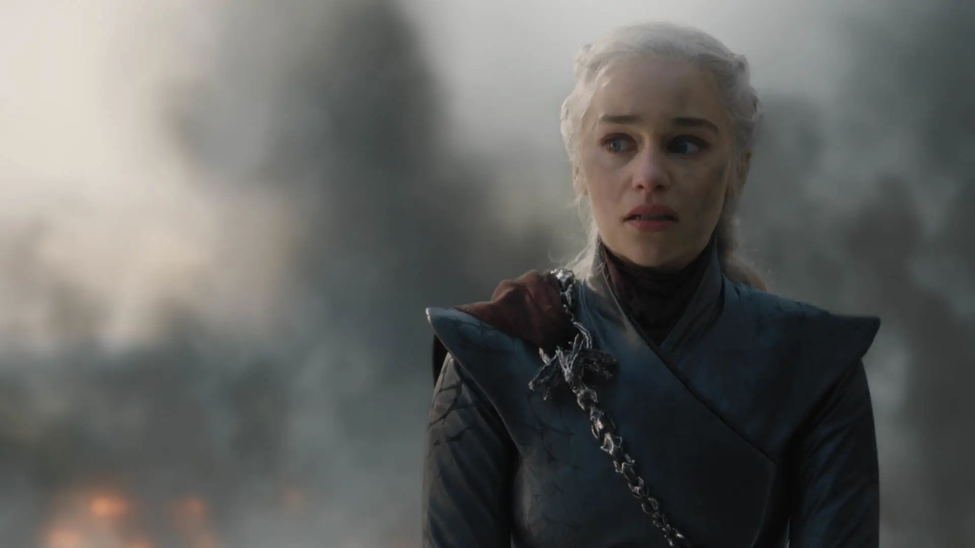emilia clark in season eight of game of thrones as daenerys targaryen. she's wearing black robes with a red cape over one shoulder, stained with soot, her white hair pulled back
