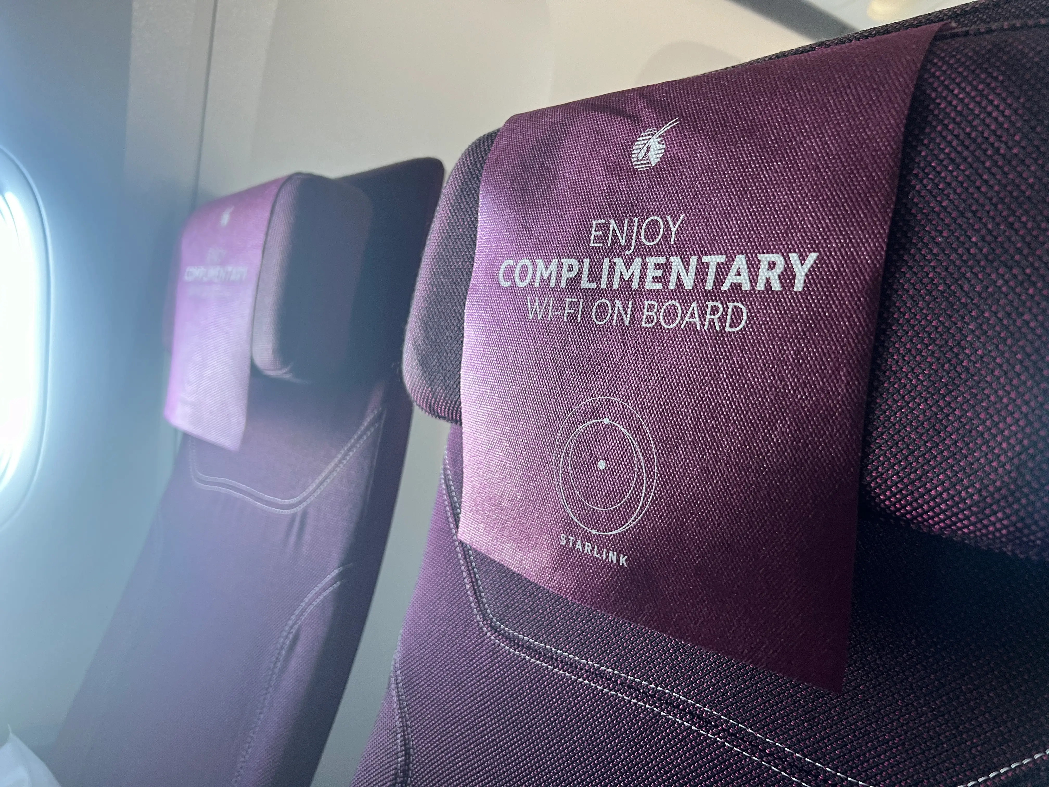 A Qatar Airways economy seat headrest with an advertisement for free Starlink WiFi