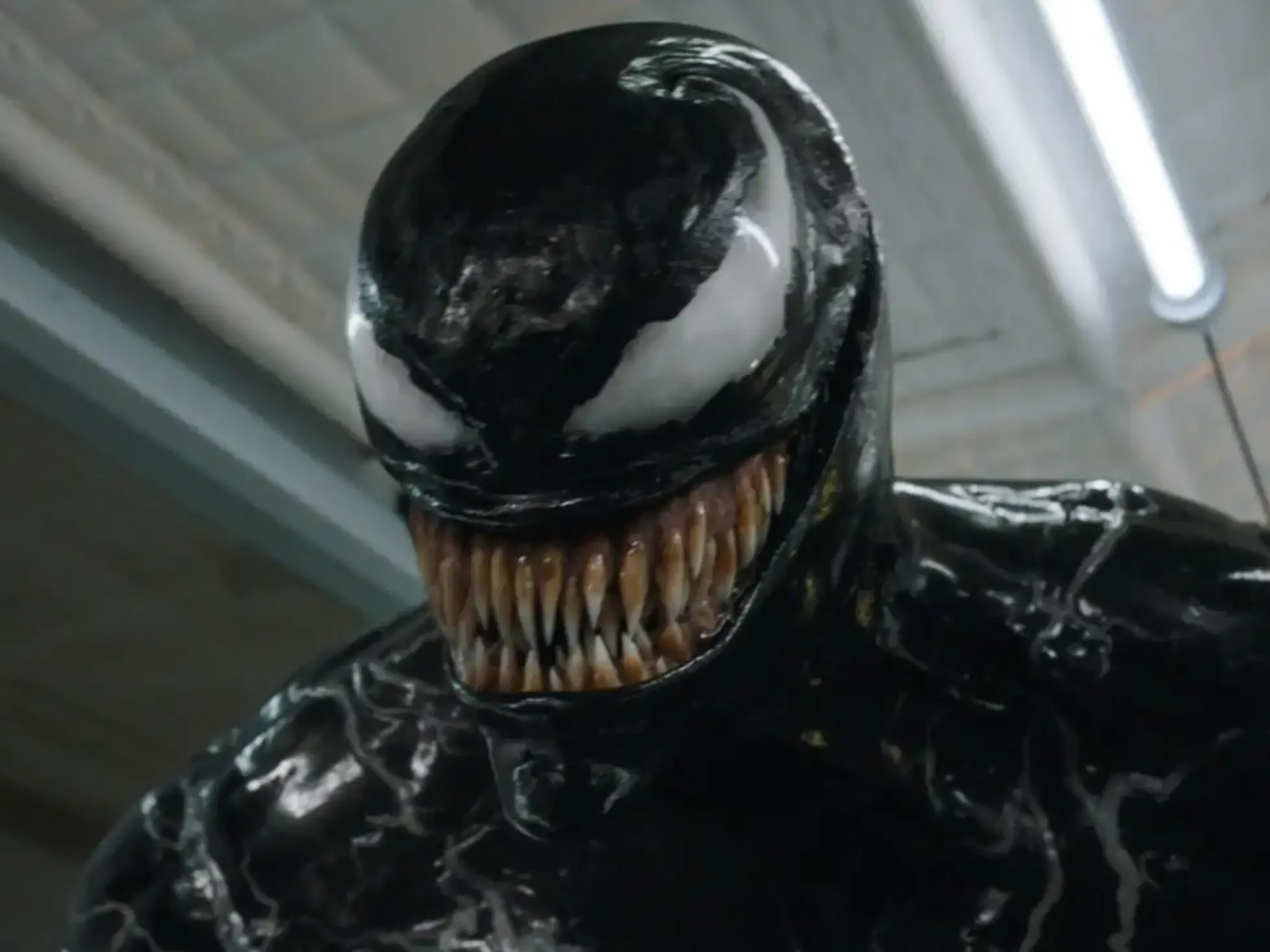 A black gooey alien with white eyes that curl up around its head. It has a large set of teeth protruding from its mouth.