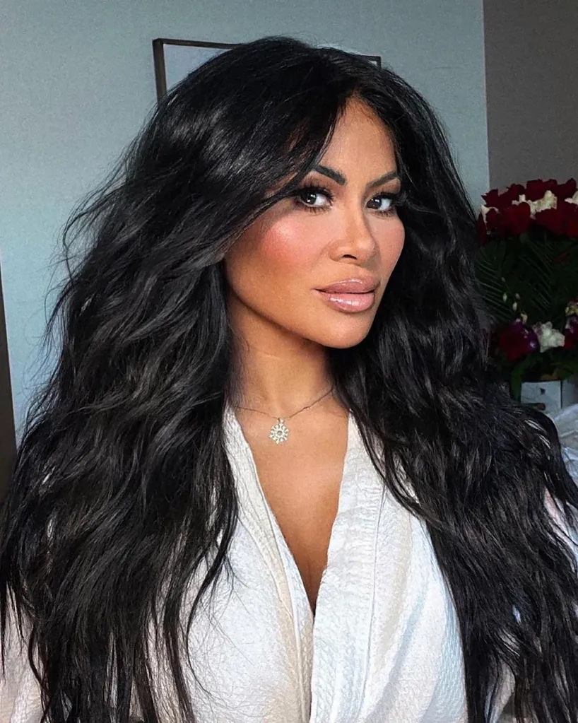A woman with long, dark, wavy hair and a light-colored robe gazes at the viewer.