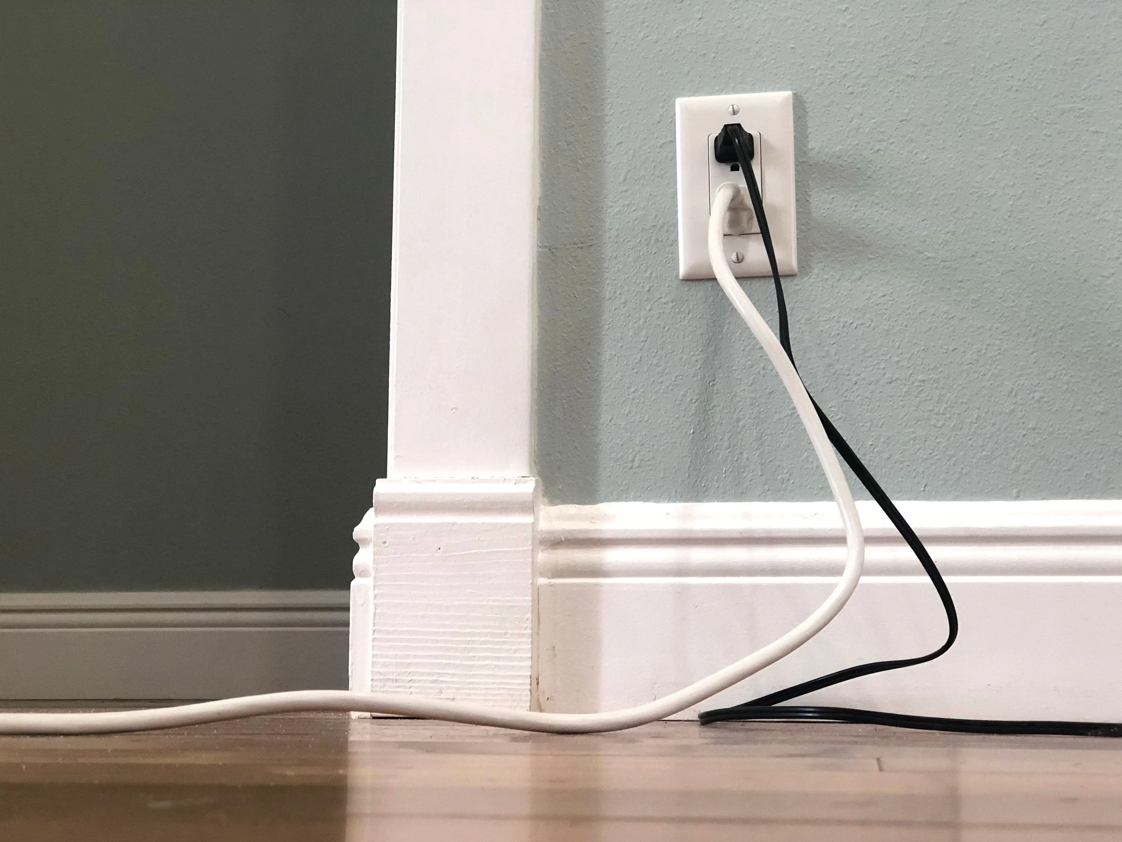 Two chunky cords plugged into an outlet on a green wall.