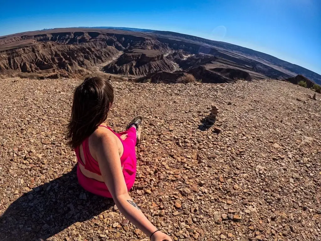 The author taking a photo of herself sitting at Fish River Canyon in Namibia. She is wearing pink and the photo is taken with her back to the camera.