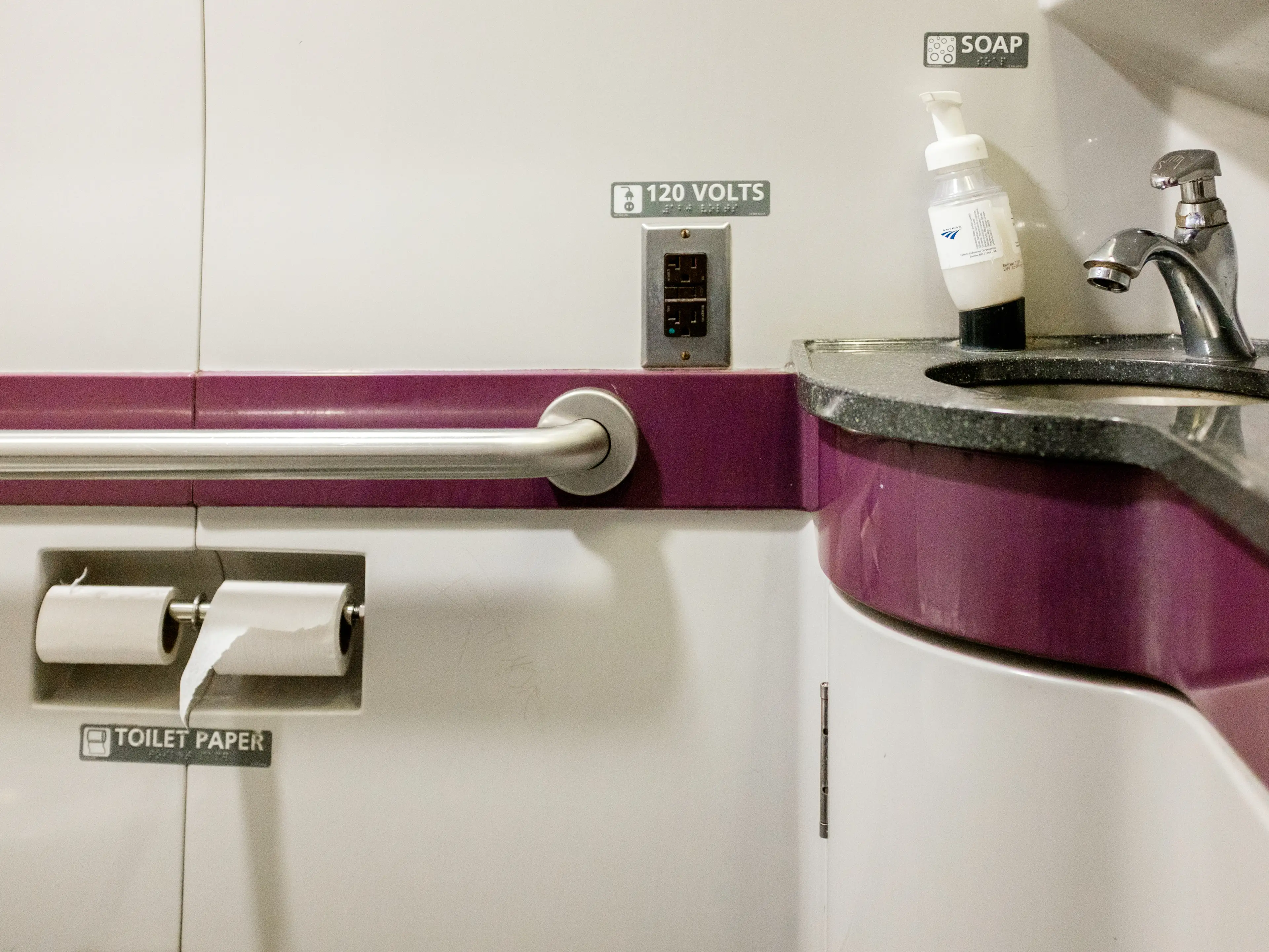 Inside a train bathroom with purple accents and a sink on the right