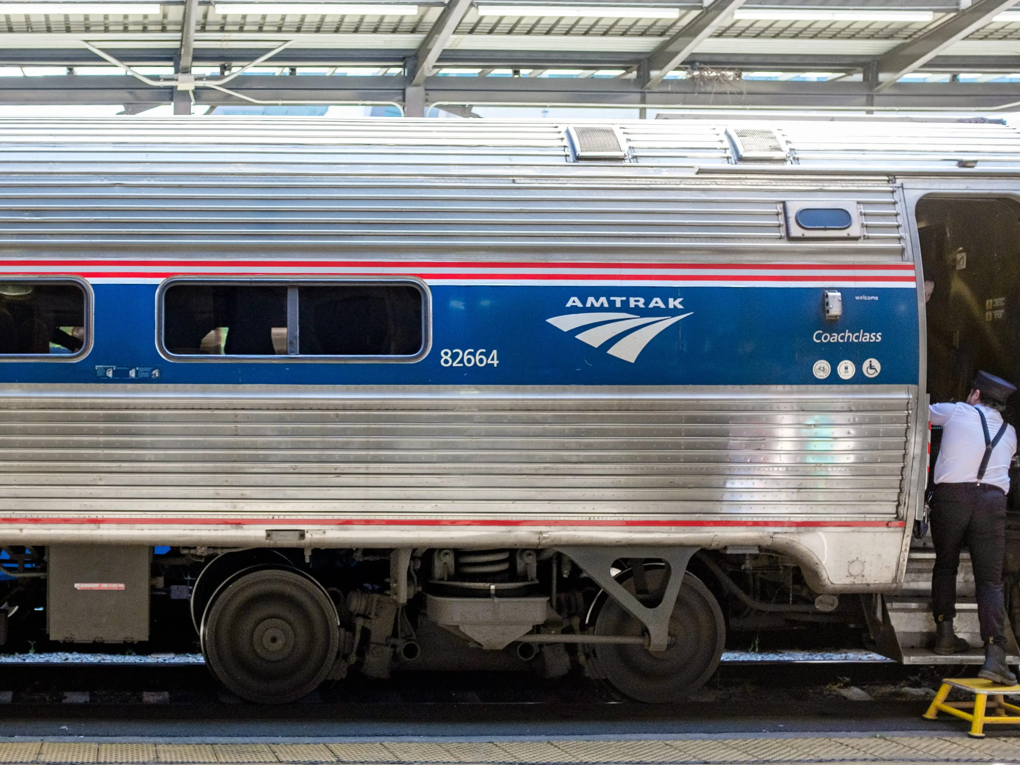 The exterior of a coach Amtrak train car with an attendant stepping into a door on the right.