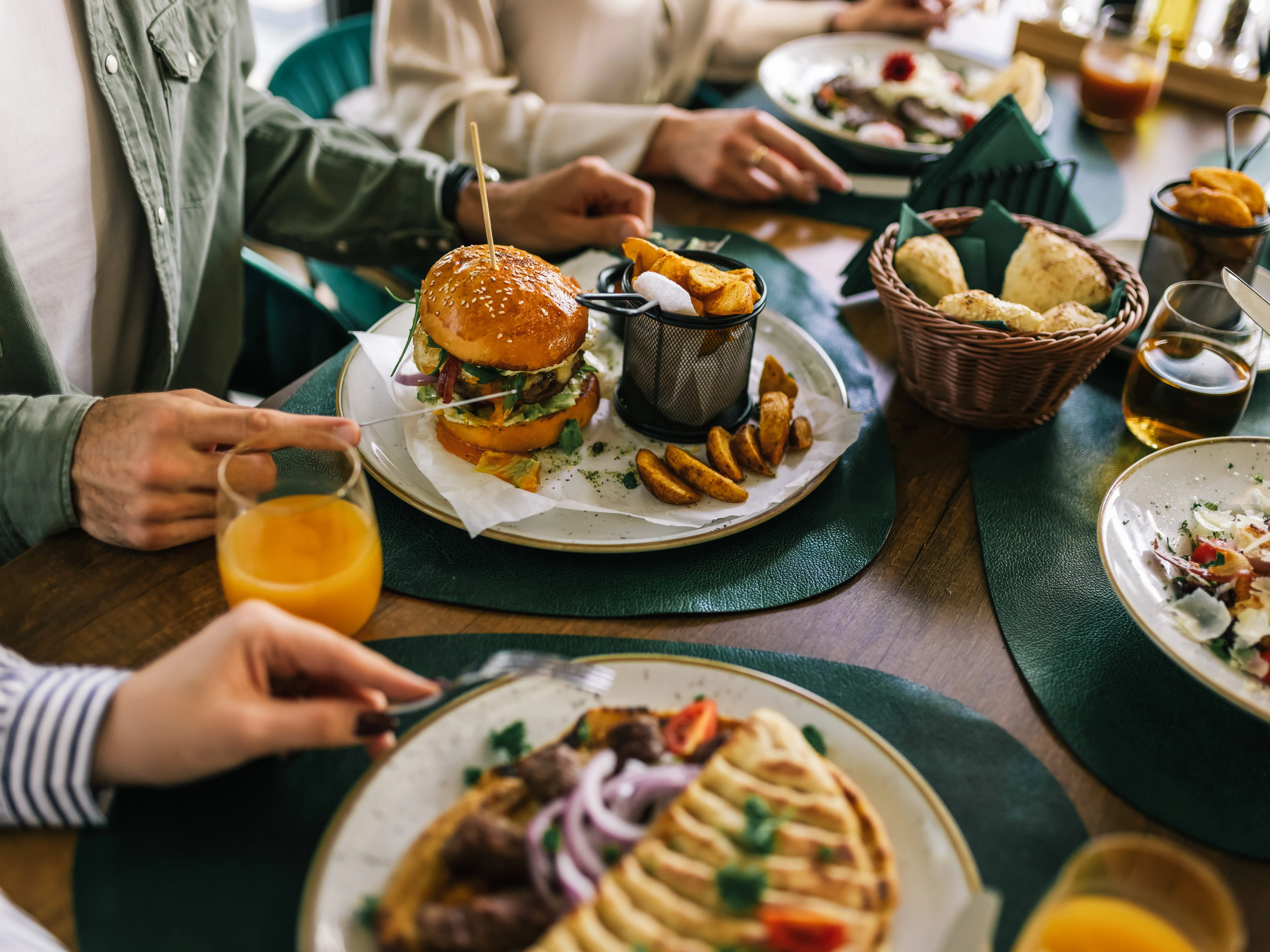A table at a restaurant covered in different dishes, with people sitting around it ready to eat.
