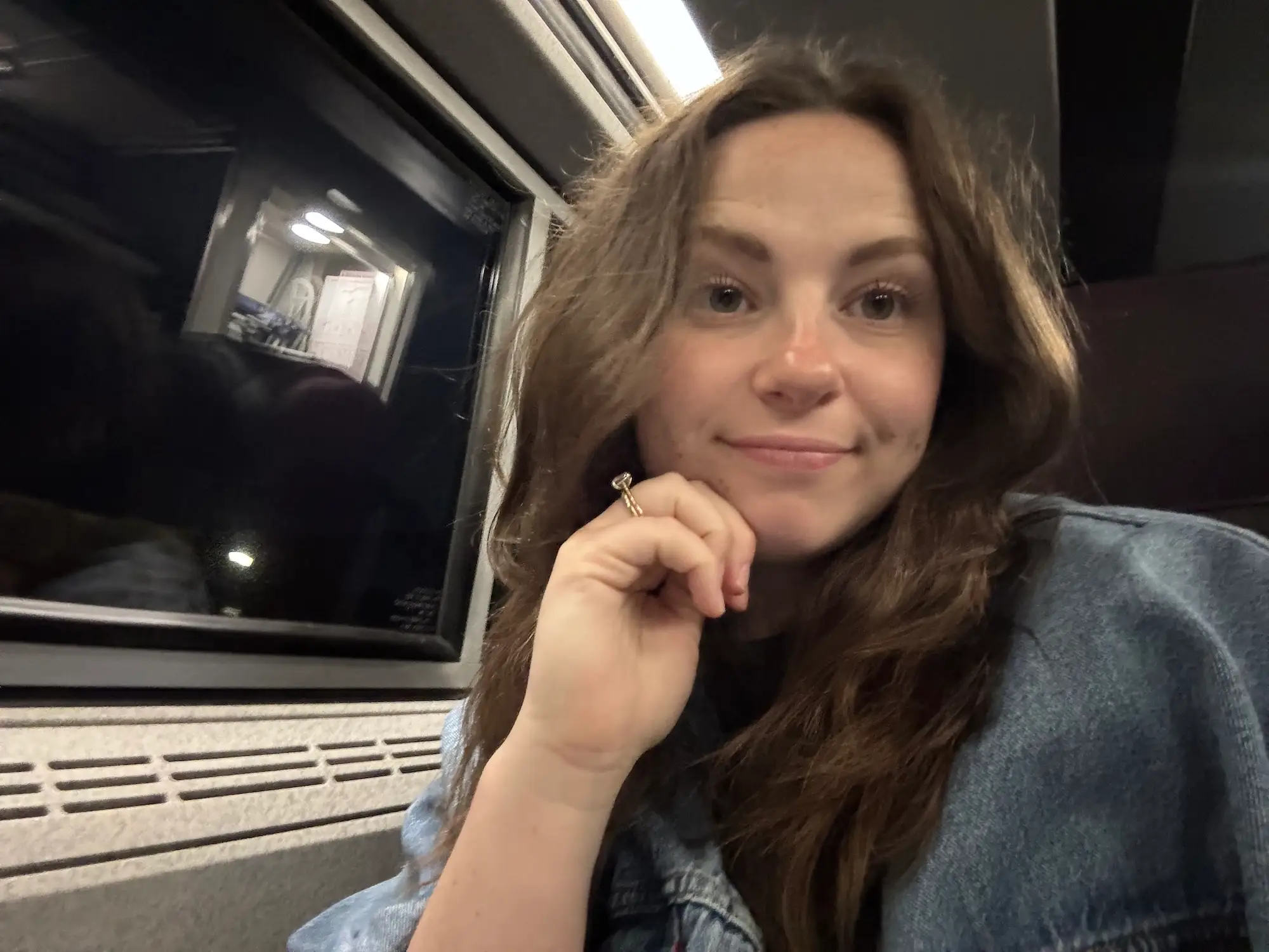 A selfie of a woman sitting on a train. It's dark outside in the nearby window.