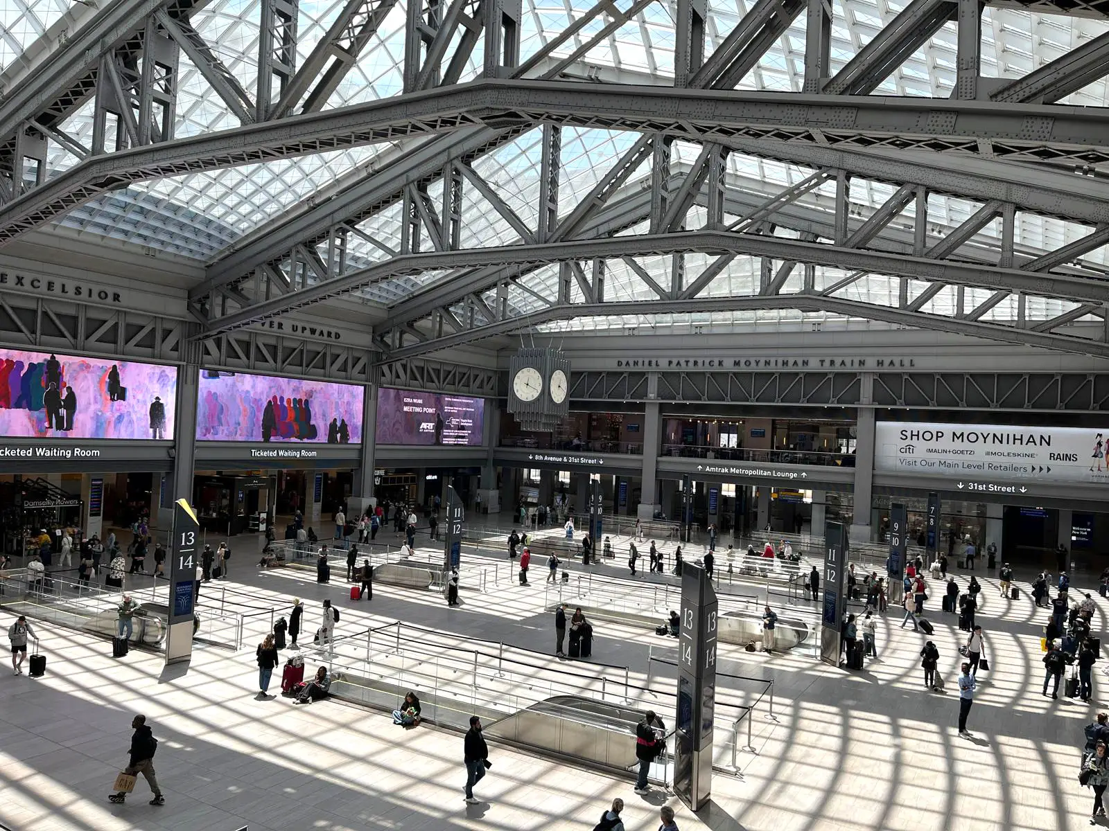 The inside of a busy train hall with shadows on the ground from the skylights.