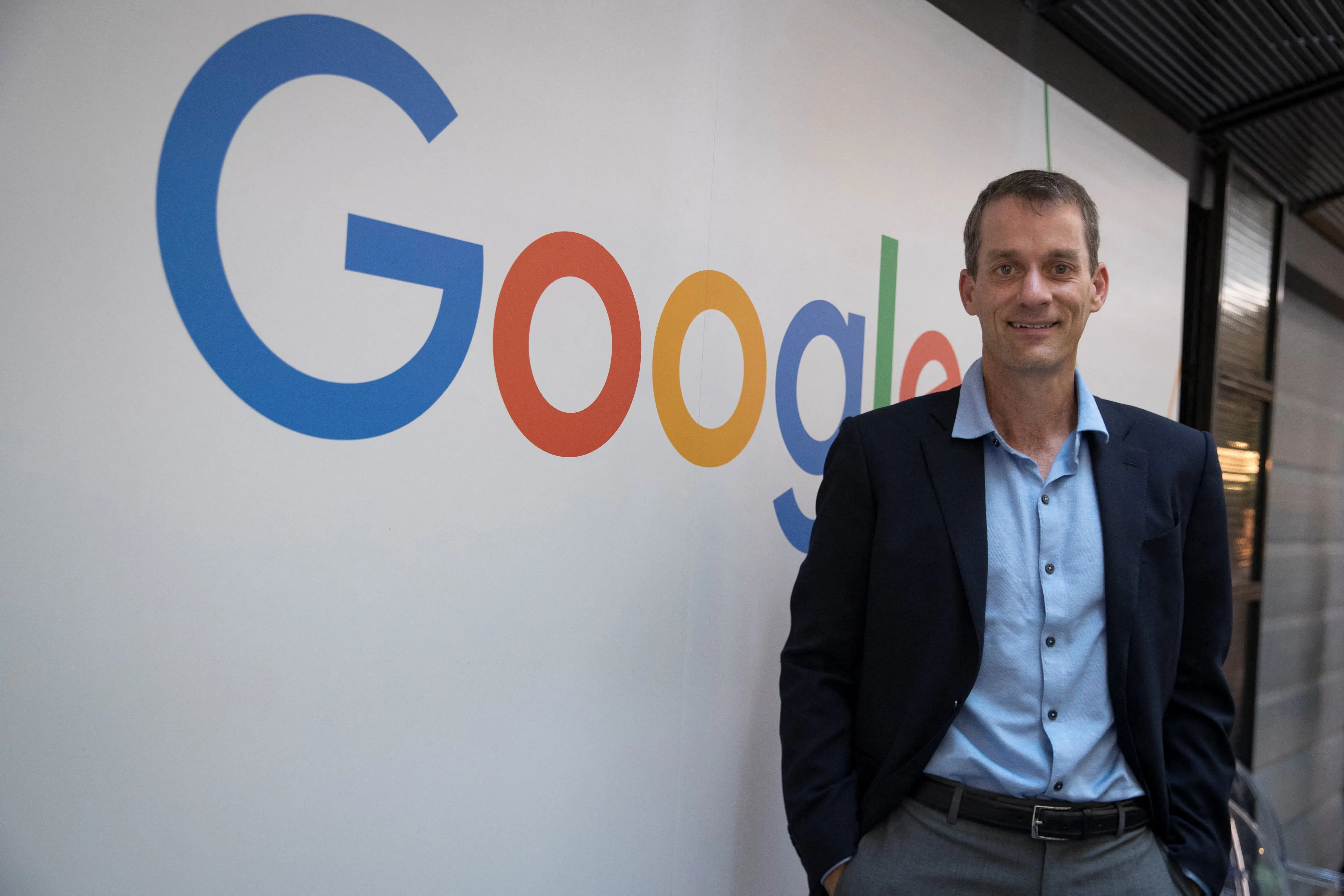 Jeff Dean stands in front of Google logo
