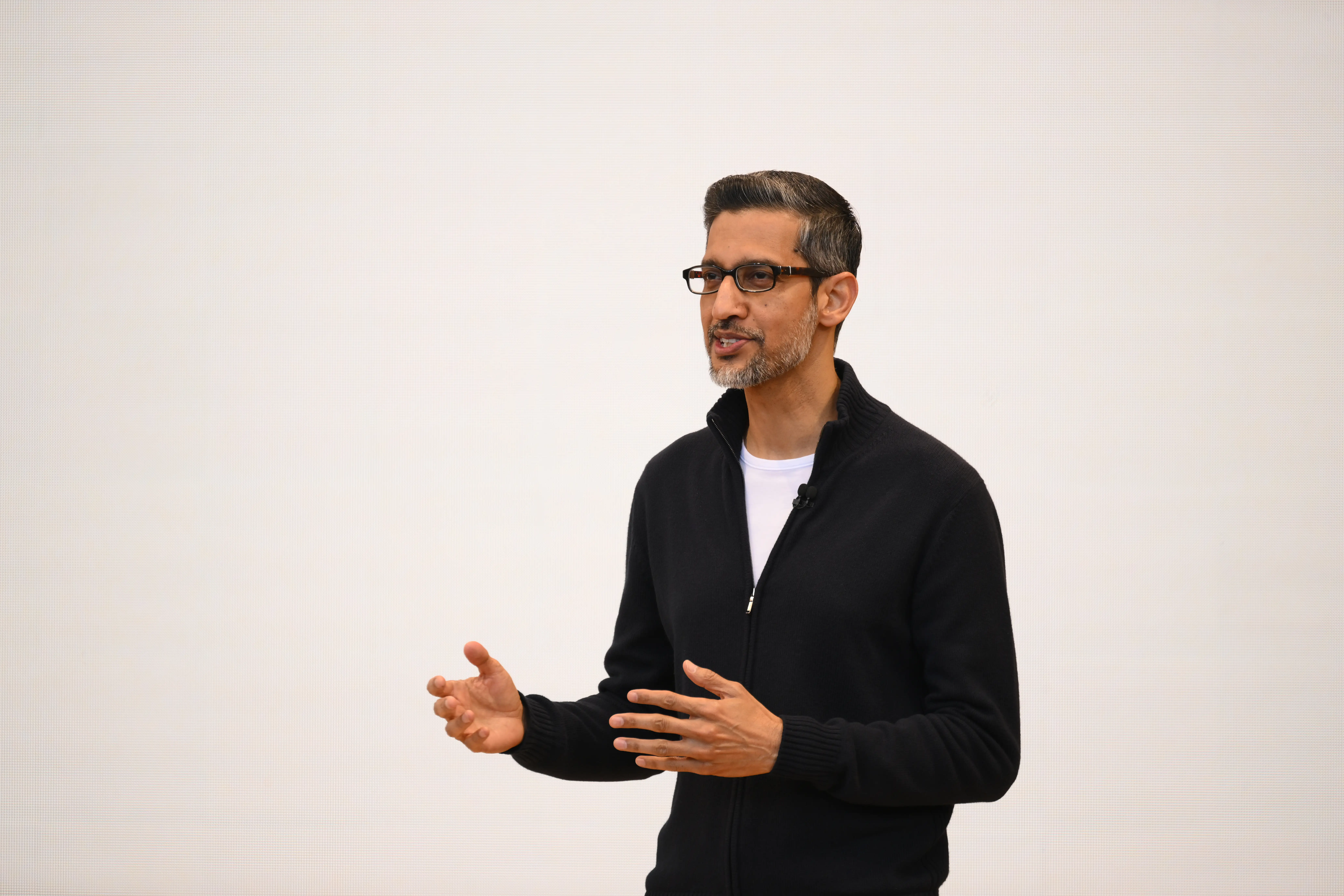 a standing man in a black quarter zip and glasses speaks