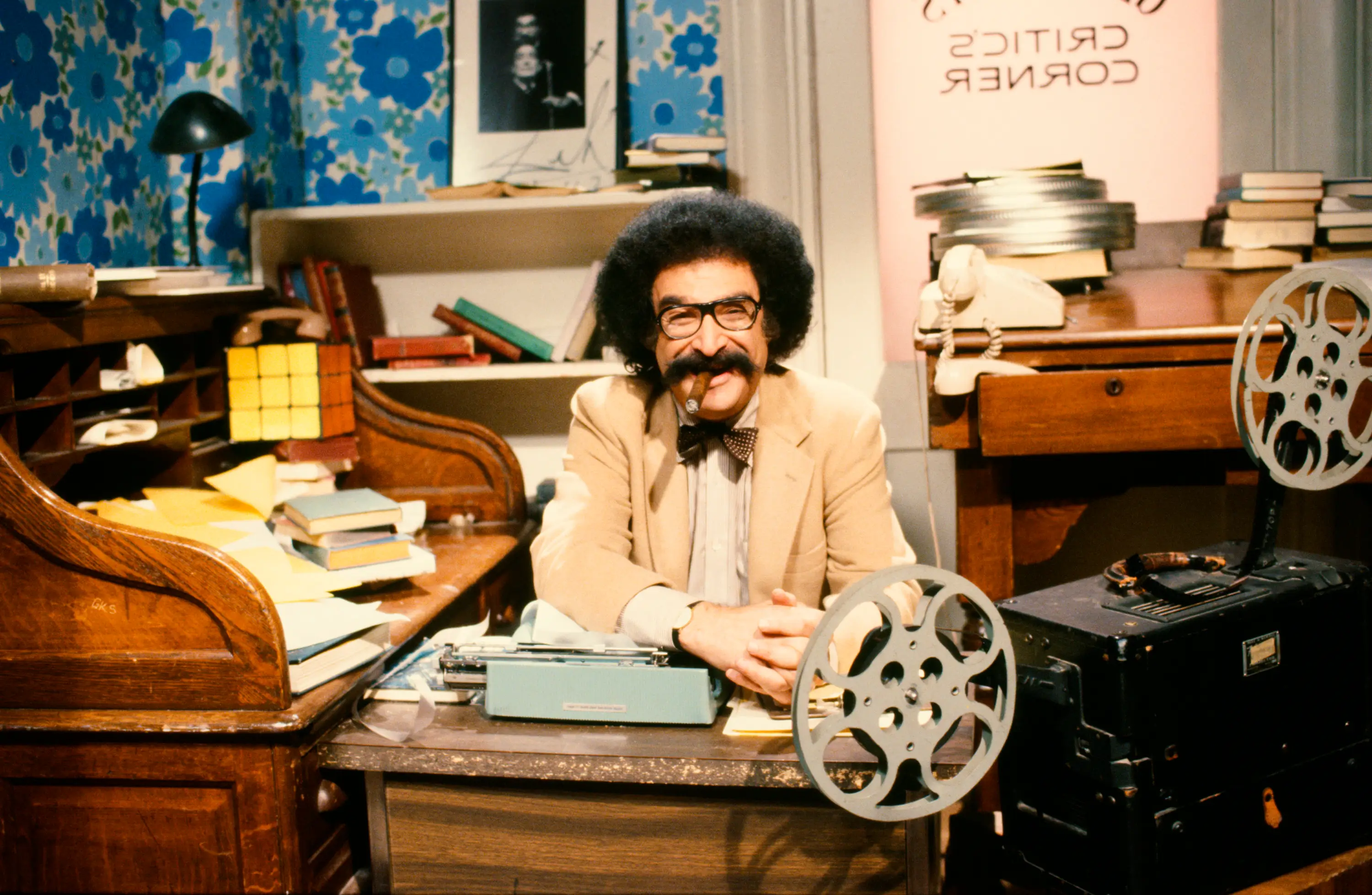 Gene Shalit sitting at desk with typwriter and movie reel