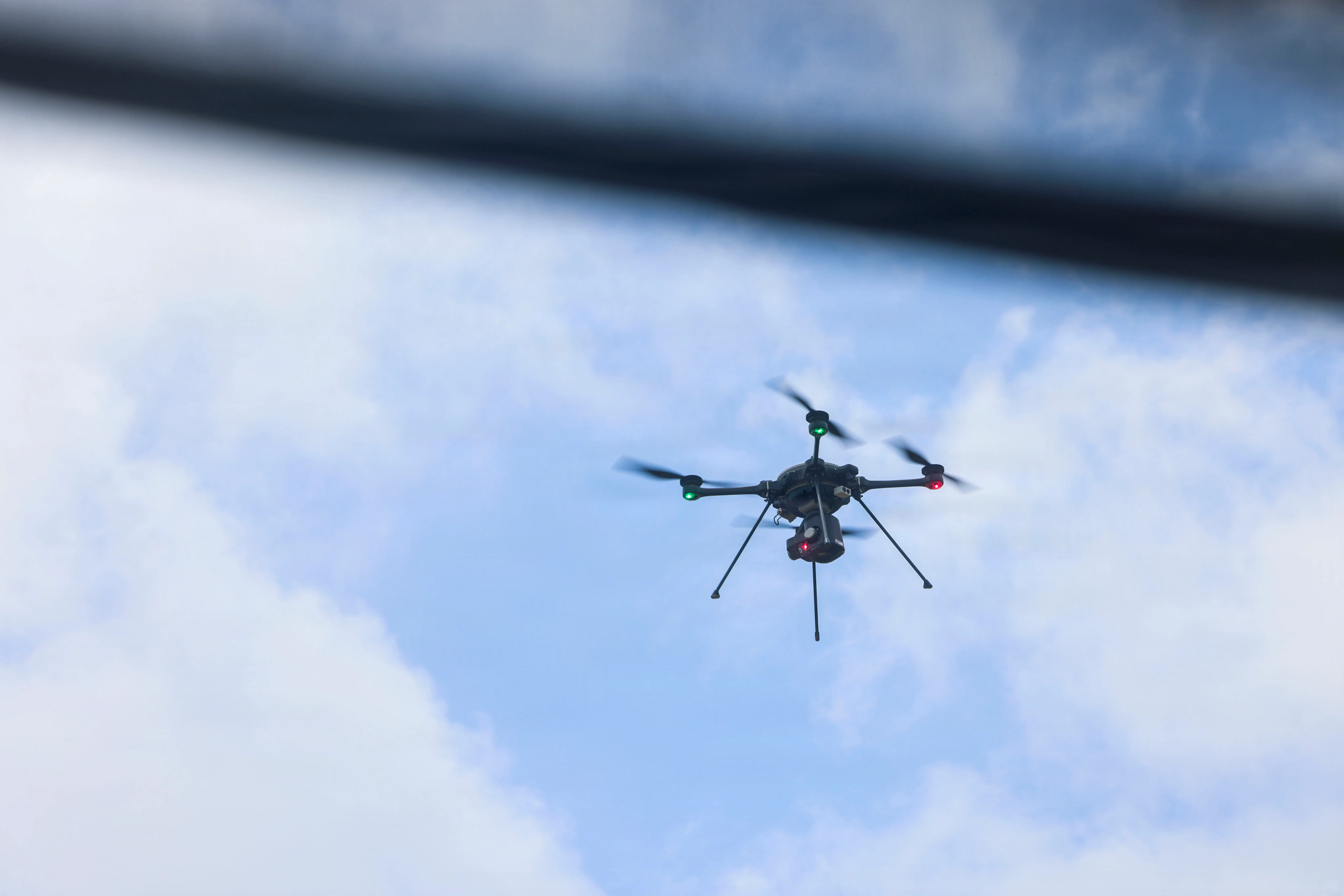 A small drone flies in a cloudy blue sky.