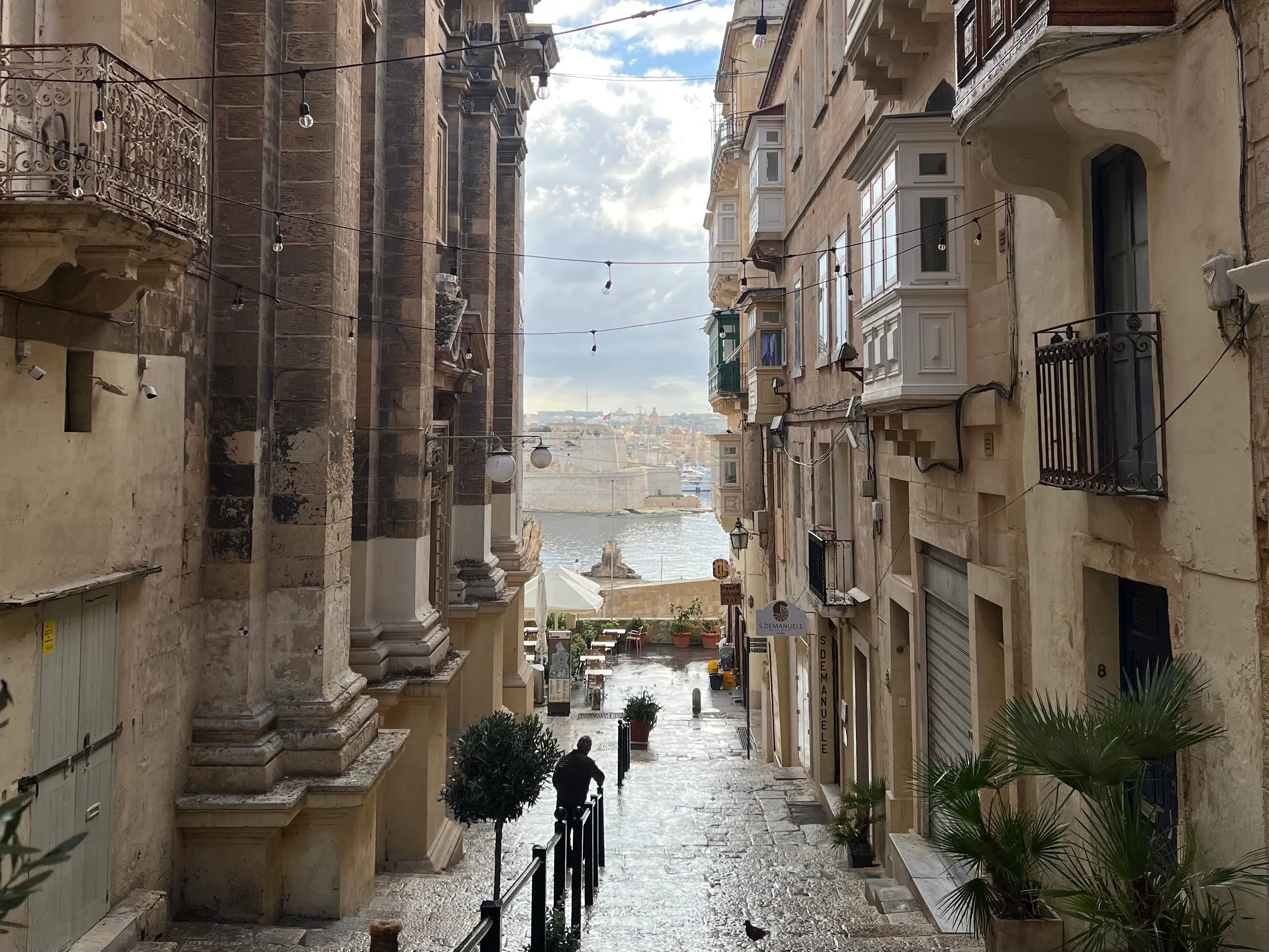 A narrow stone street lined with buildings near the waterfront in Malta.