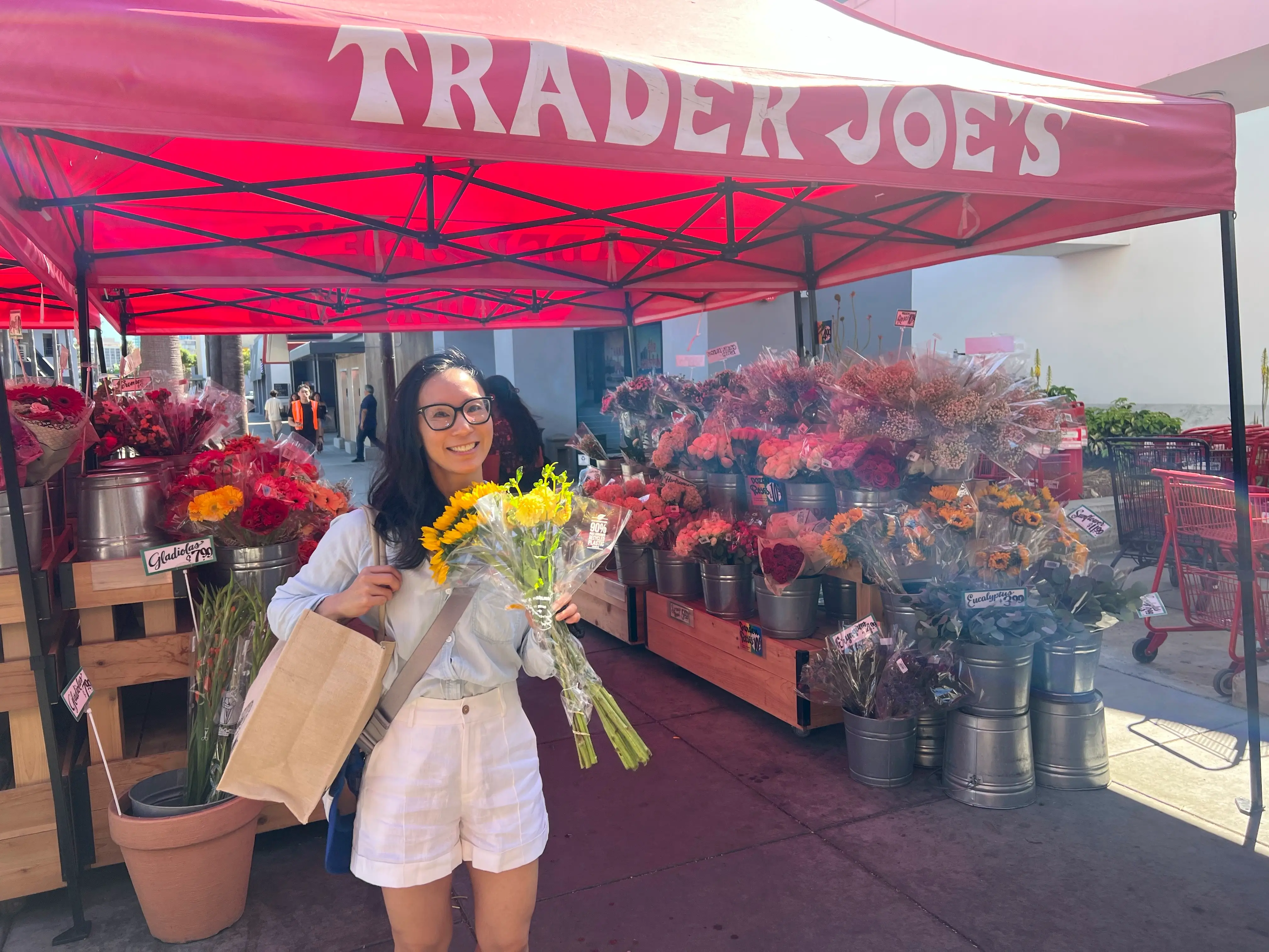 Woman holding flowers under Trader Joe's awning, smiling