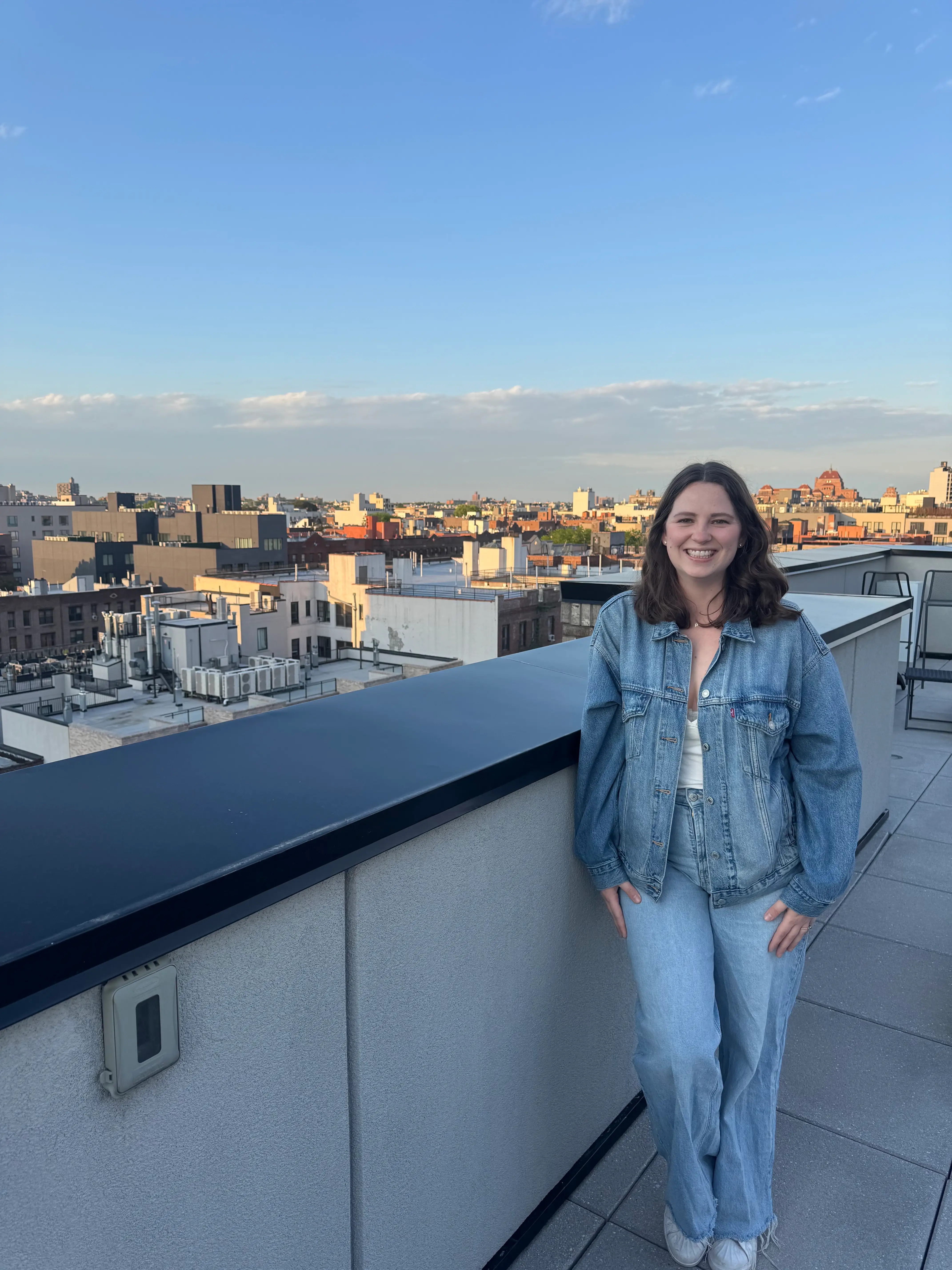A woman smiles on a rooftop with a city skyline behind her.