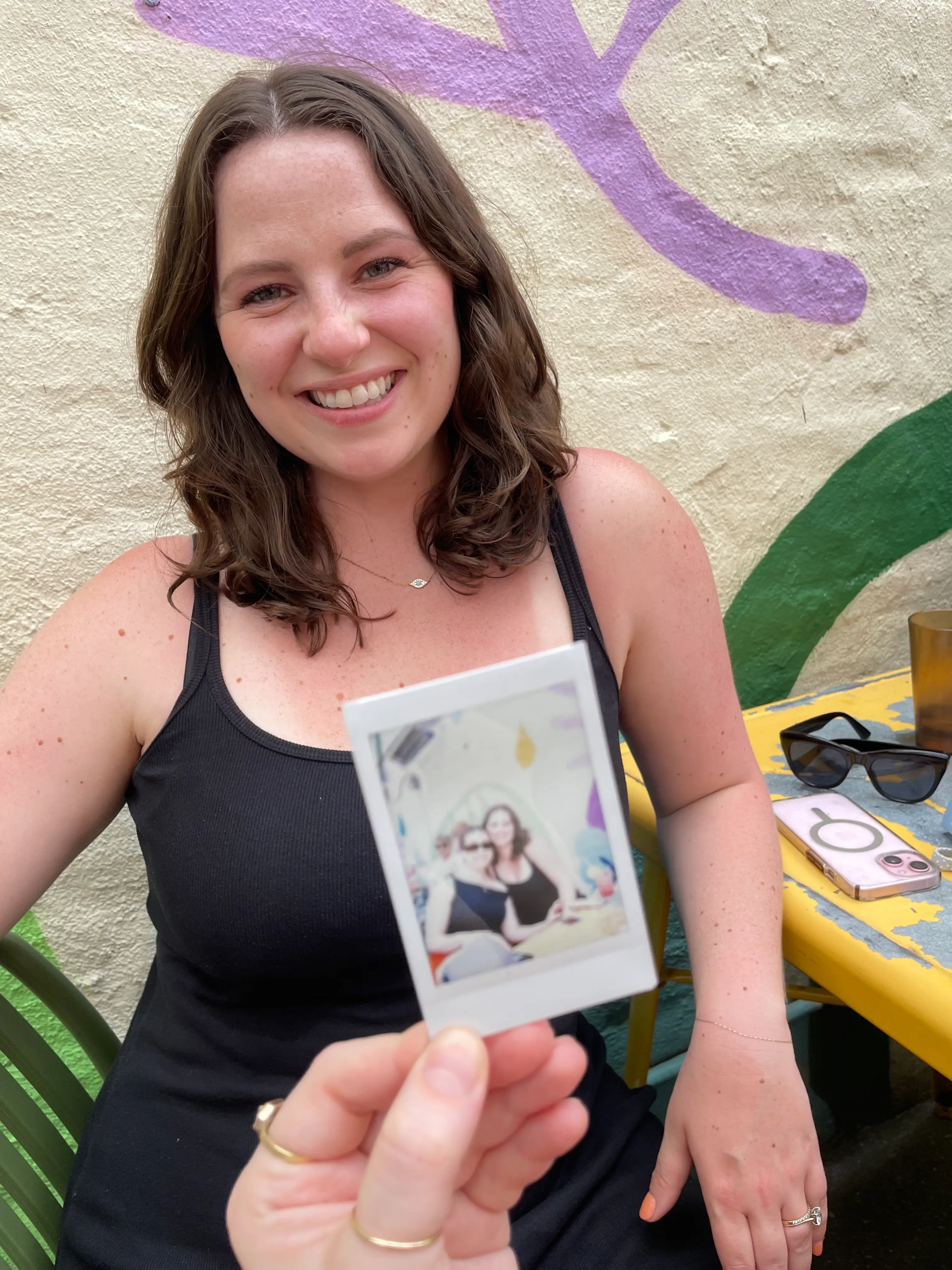 A woman smiles as a person holds a Polaroid photo in front of her.