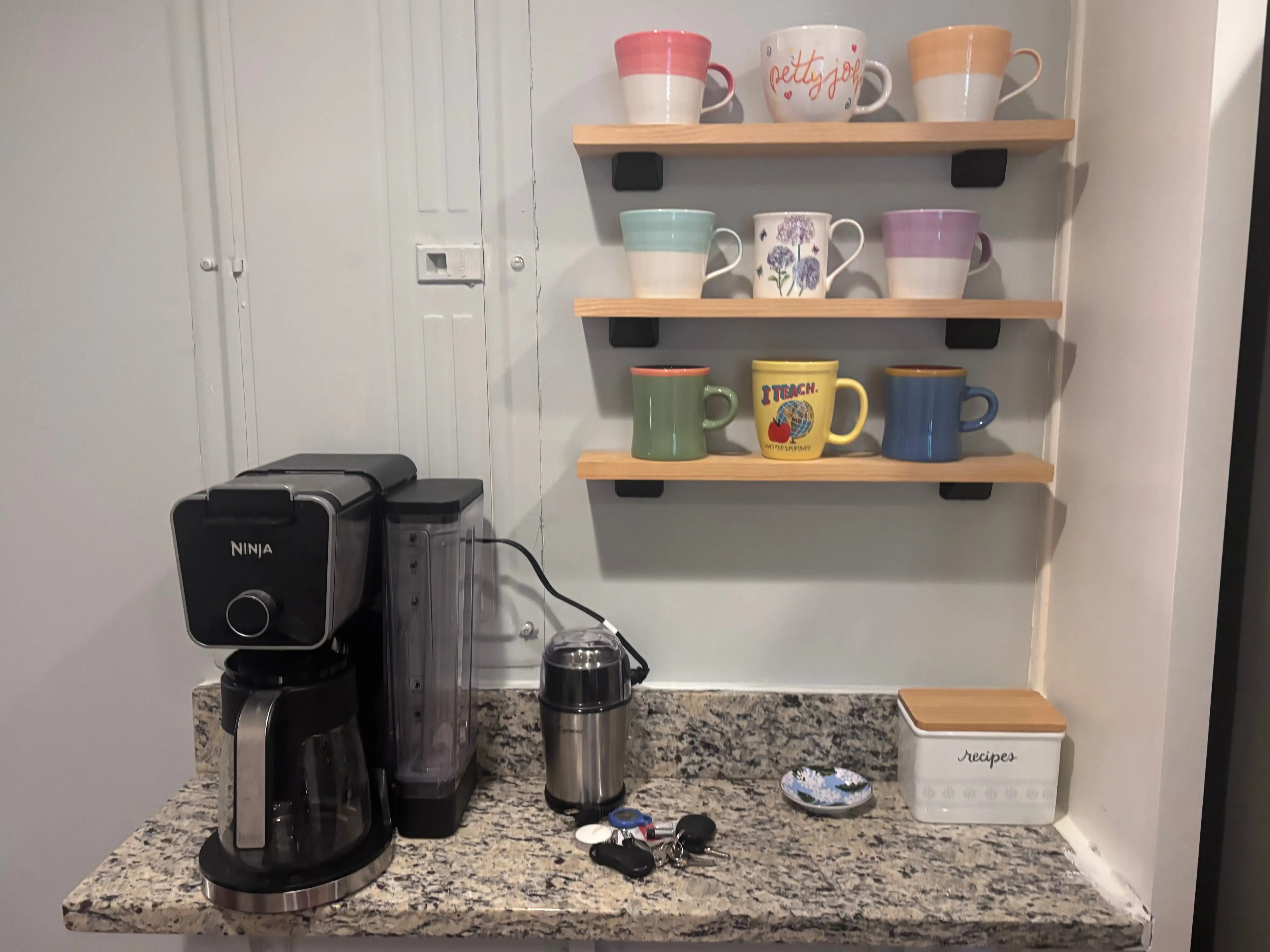 A coffee bar in a kitchen with mugs on floating shelves above it.