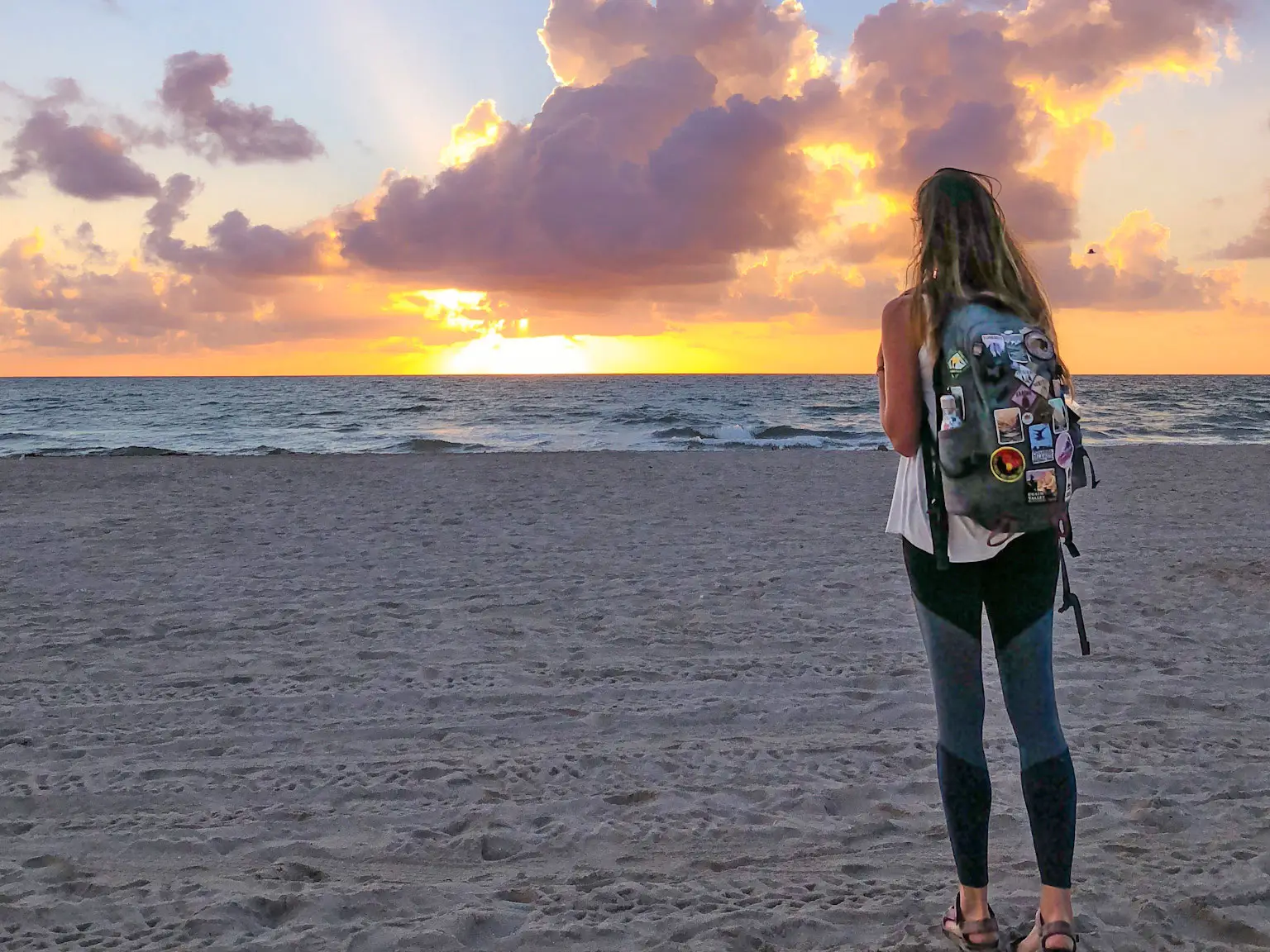 Emily stands on a beach, looking out at the water at sunrise.