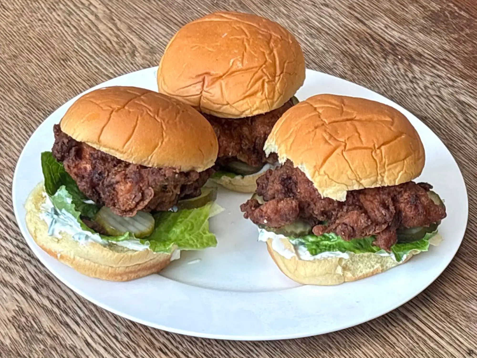 Three fried-chicken sandwiches on a white plate.