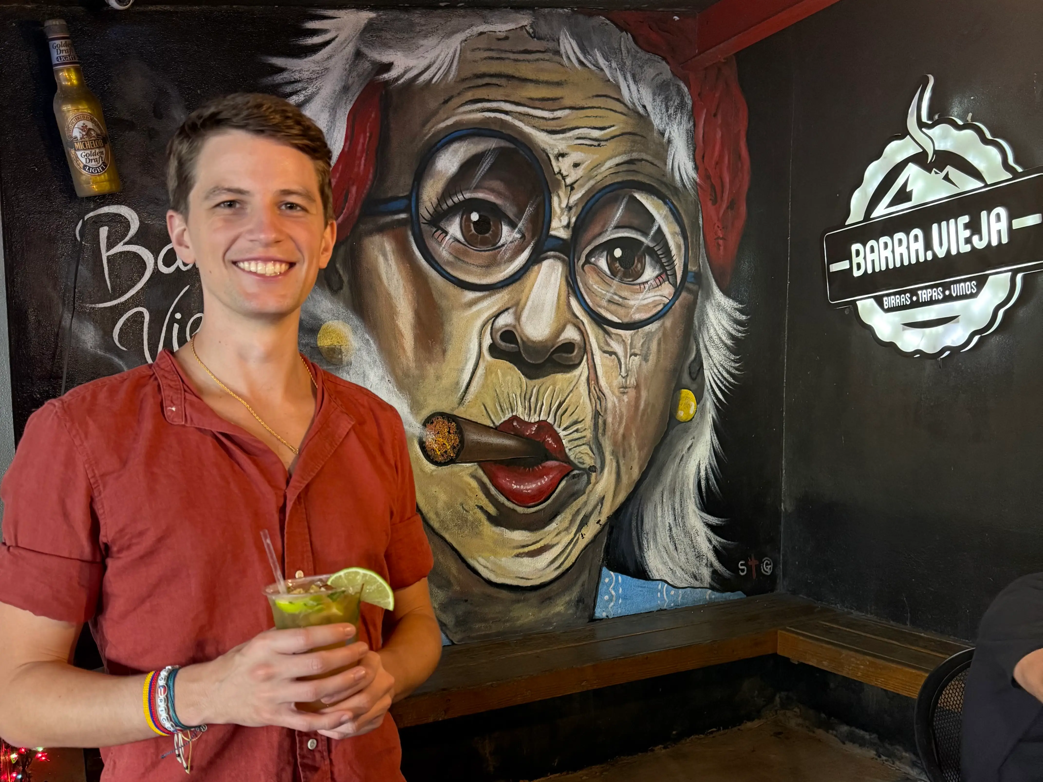 Man smiling with drink in front of artwork