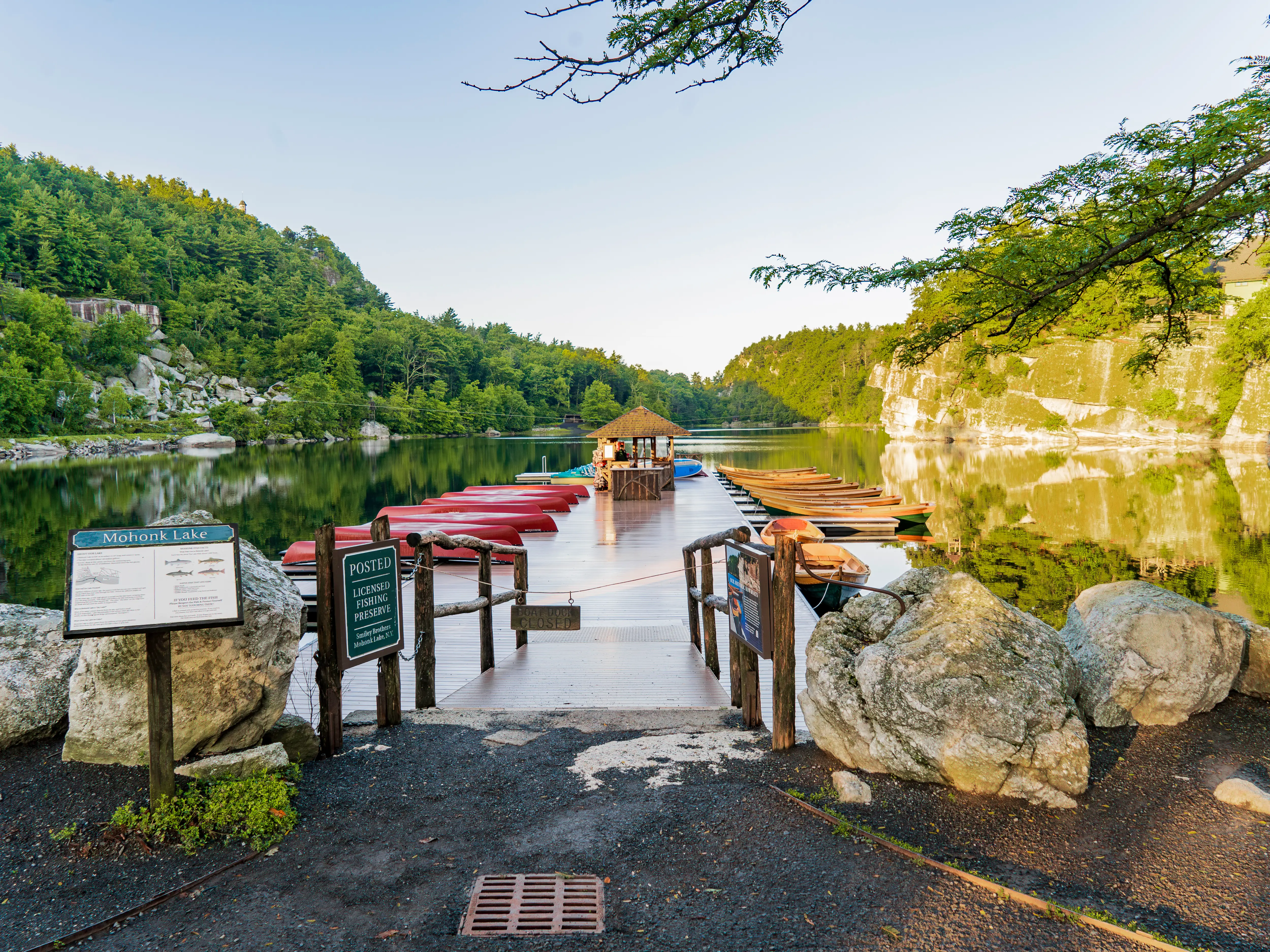 Wooden dock with canoes and rowboats extends into Mohonk Lake amid forested cliffs and calm reflections.
