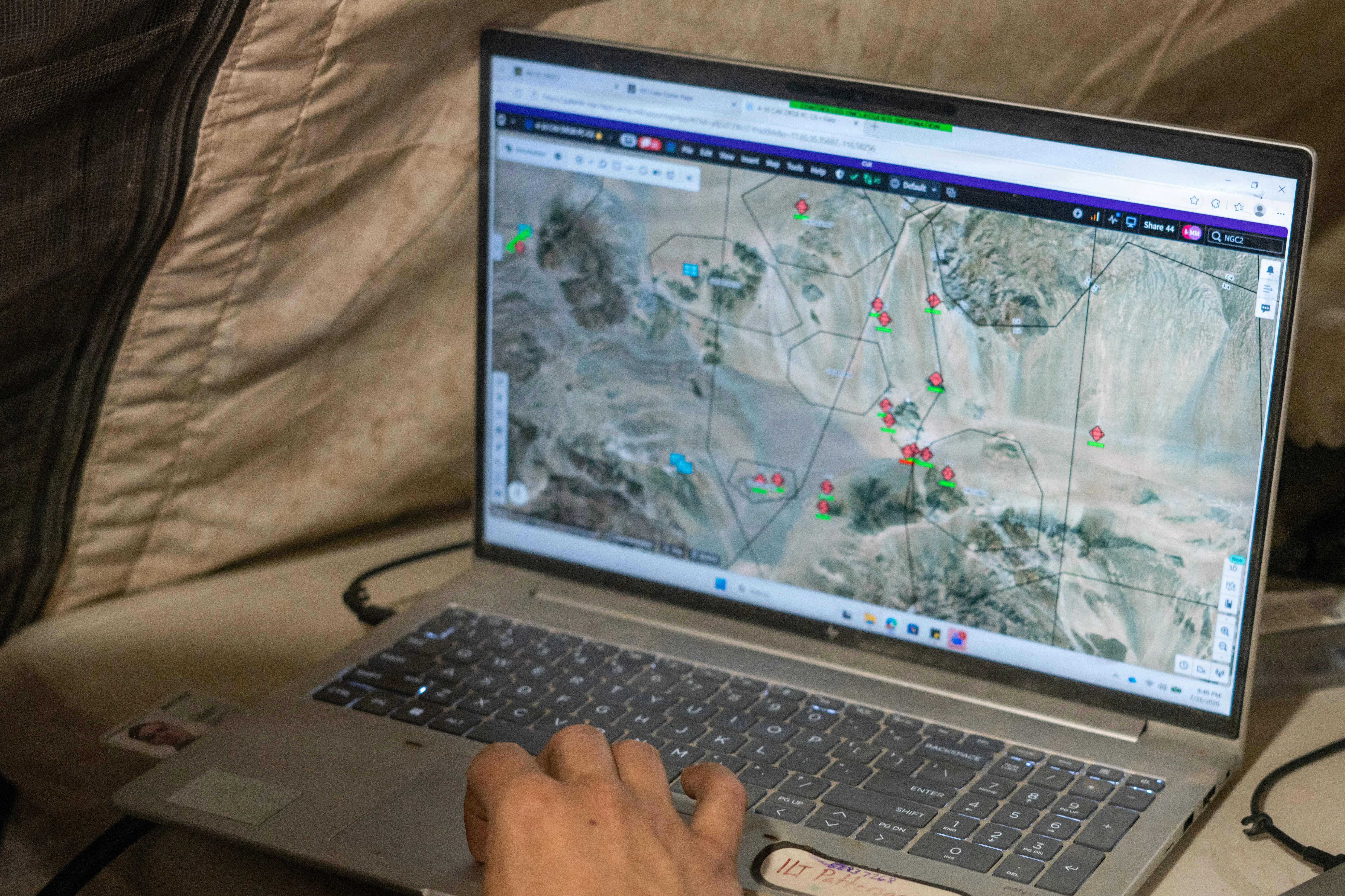 A laptop shows a map with blue and red dots on a landscape.