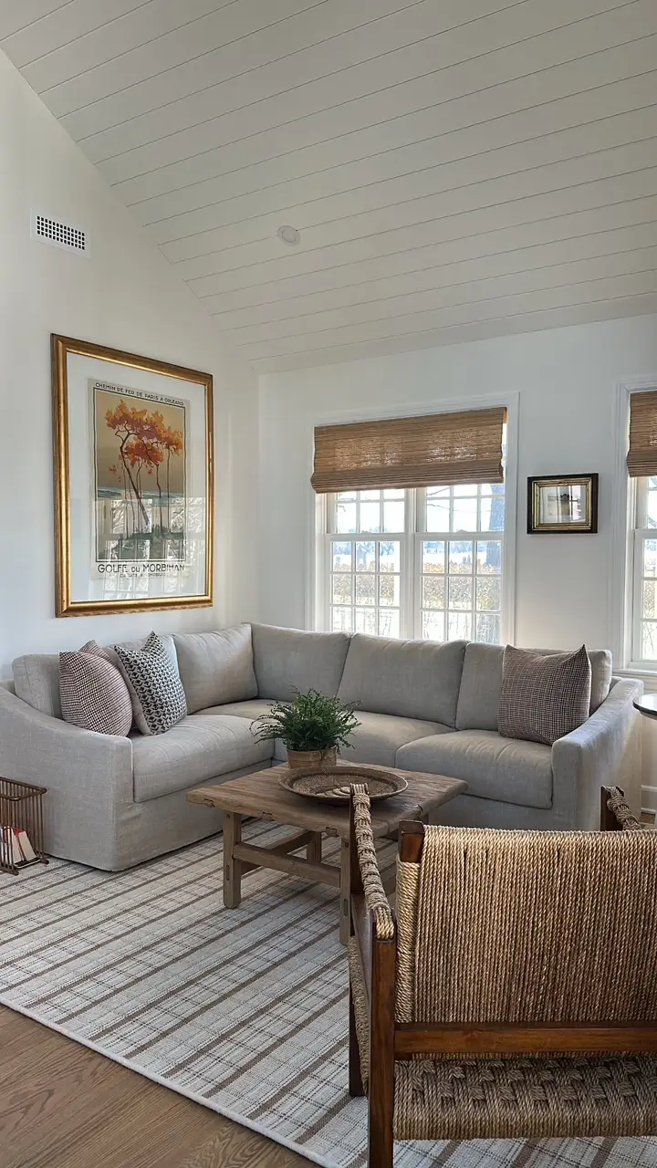 Bright living room with a gray sectional sofa, woven blinds, framed wall art, and a rustic coffee table.