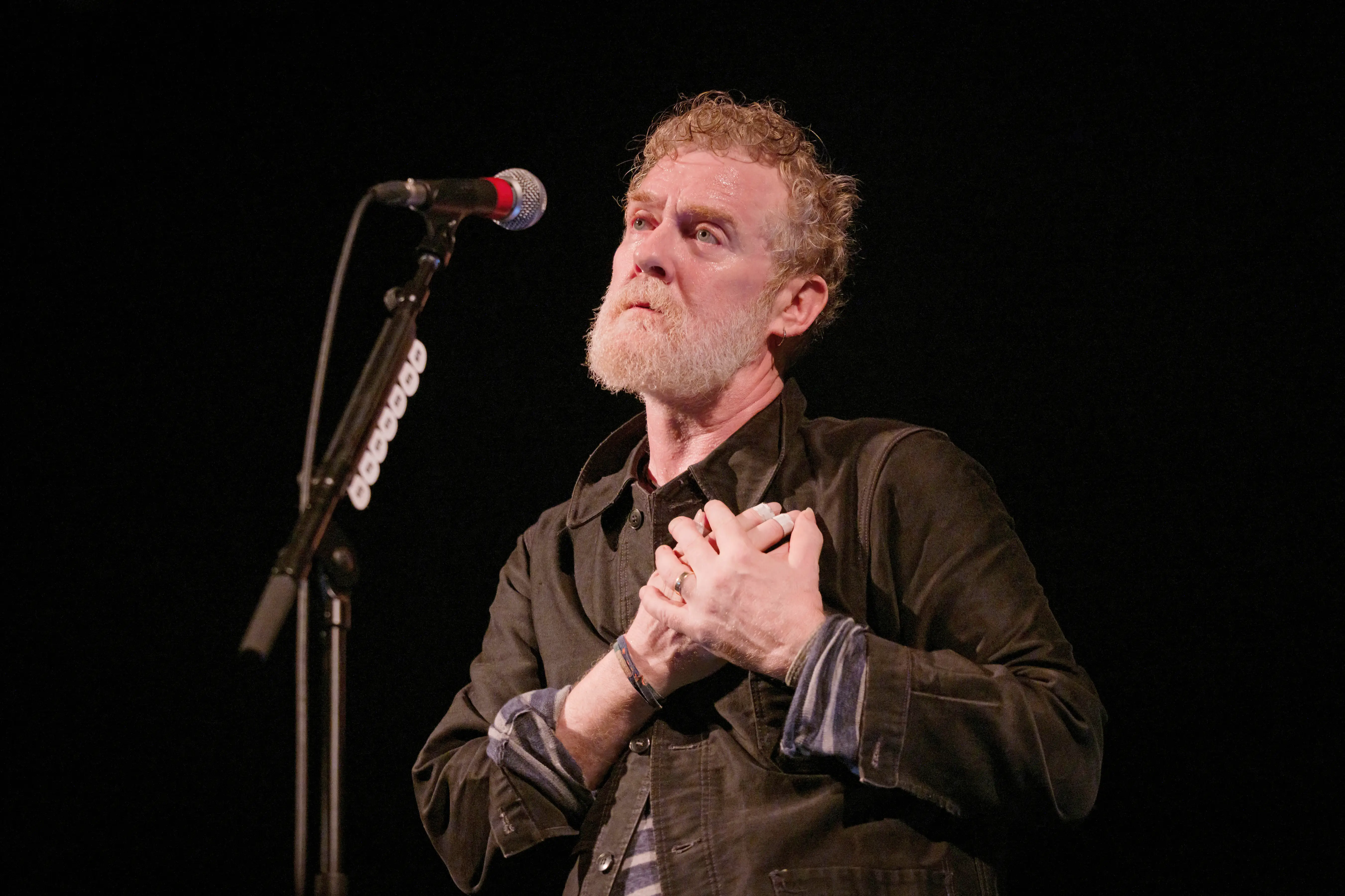 Glen Hansard holding his hands to his heart next to a microphone
