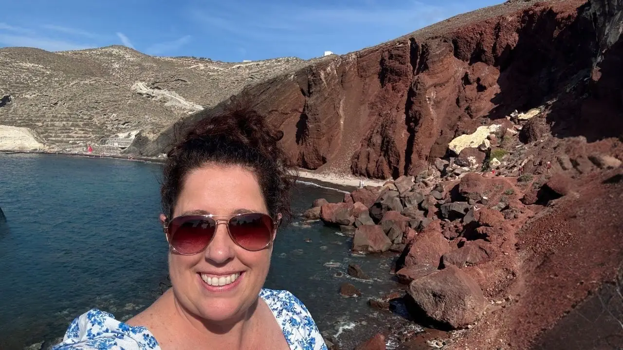 Woman smiling next to water, cliffs in Santorini