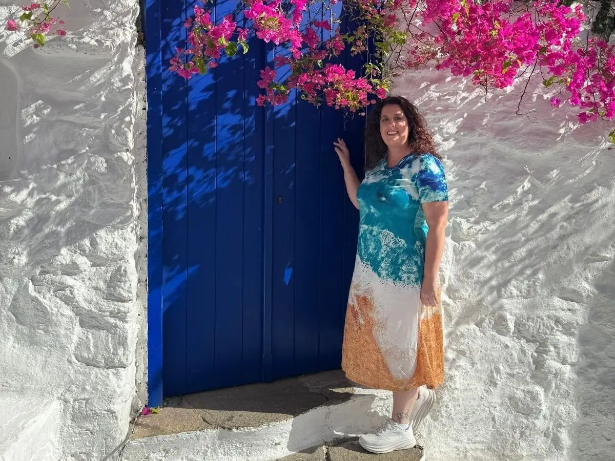 Woman smiling under pink flowering tree and in front of blue door in Mykonos