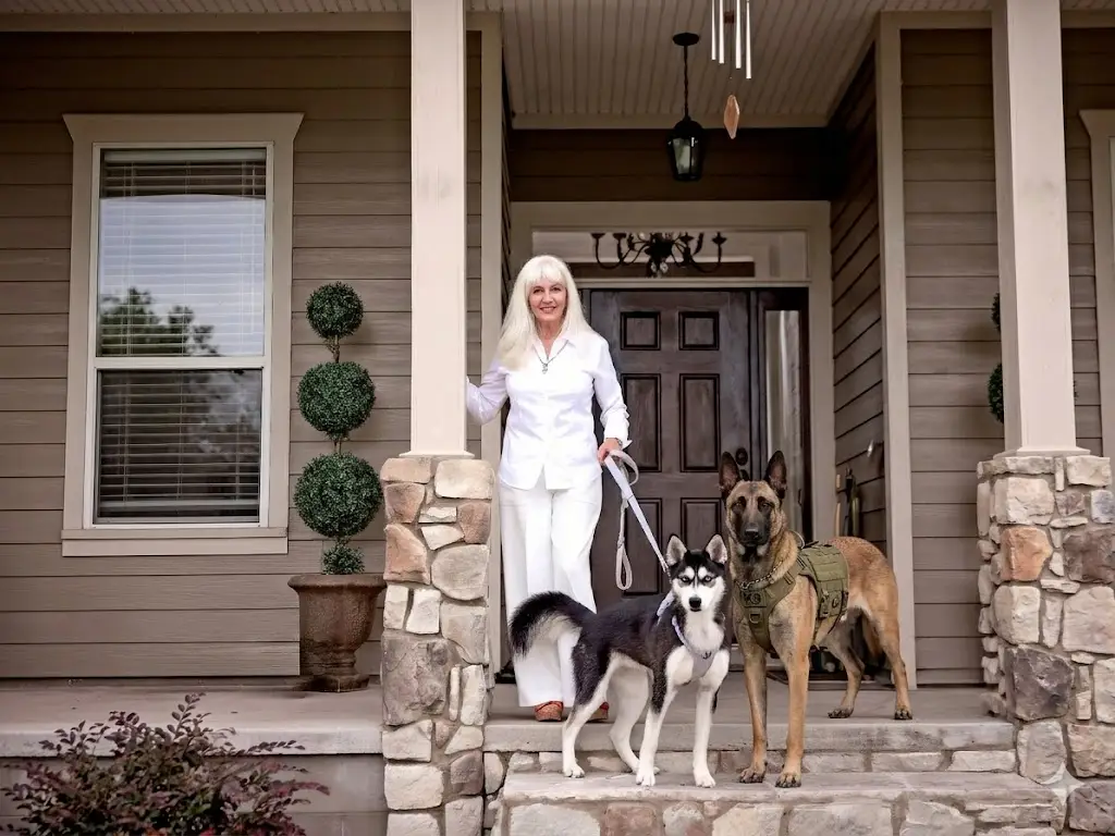 a woman poses on her porch with two dogs