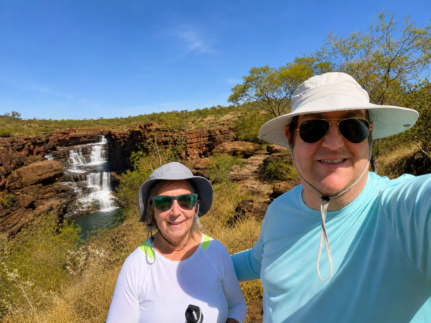 Man and woman smiling with waterfalls, trees in background