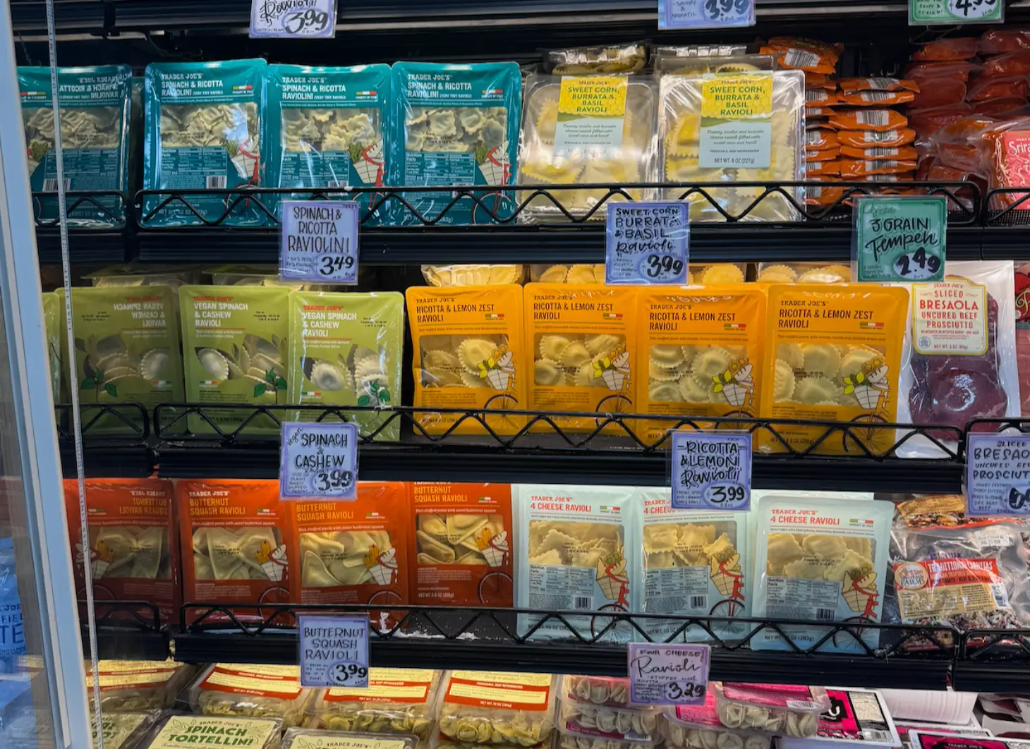 Refrigerated Trader Joe’s shelf displays packaged ravioli varieties with handwritten price signs.