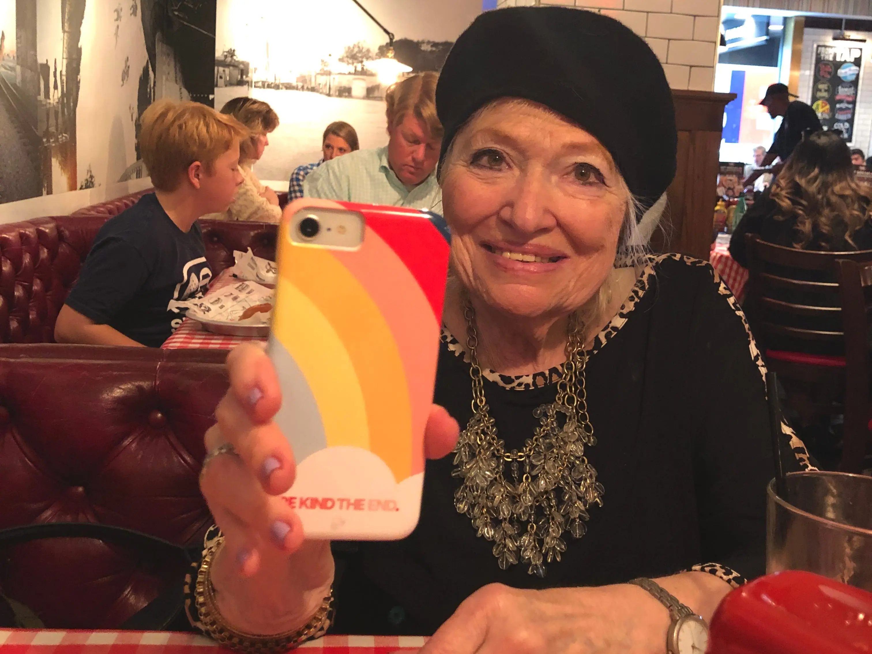 The author's mother holds up a cell phone while in a restaurant.