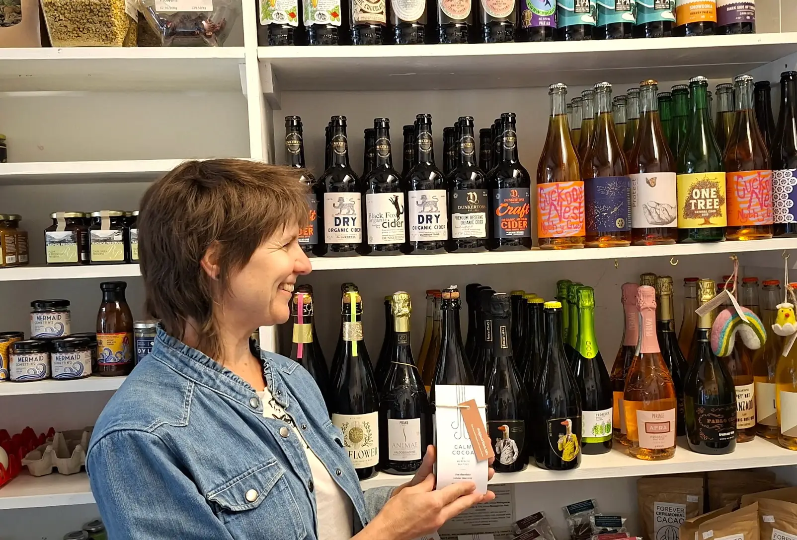 The writer holding a bag of hot chocolate in front of wines at a local store.
