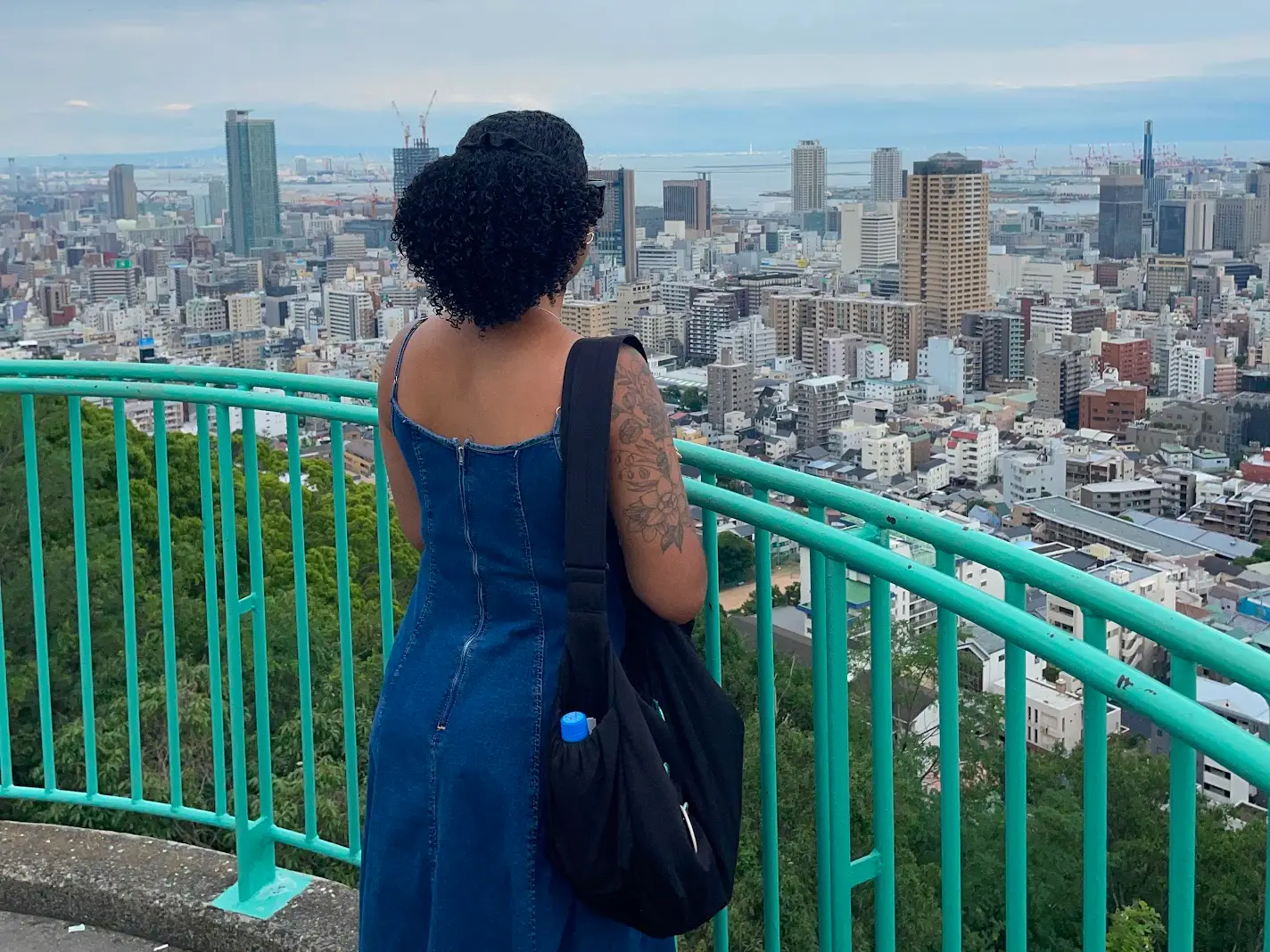 Woman iin front of green railing staring at Japan skyline