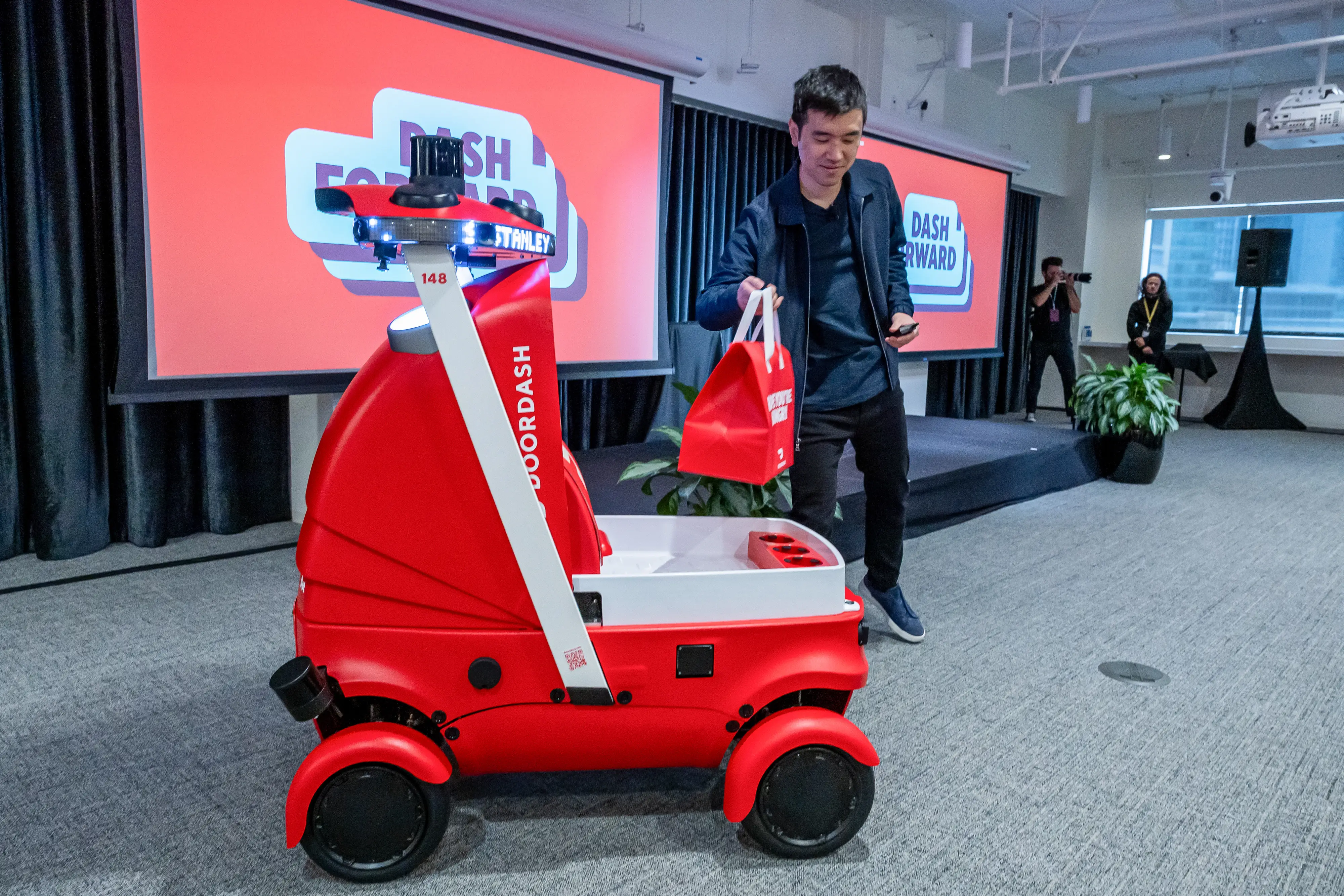 A man puts a red-and-white DoorDash bag into Dot, DoorDash's red-and-white wheeled delivery robot, during a presentation at DoorDash headquarters.