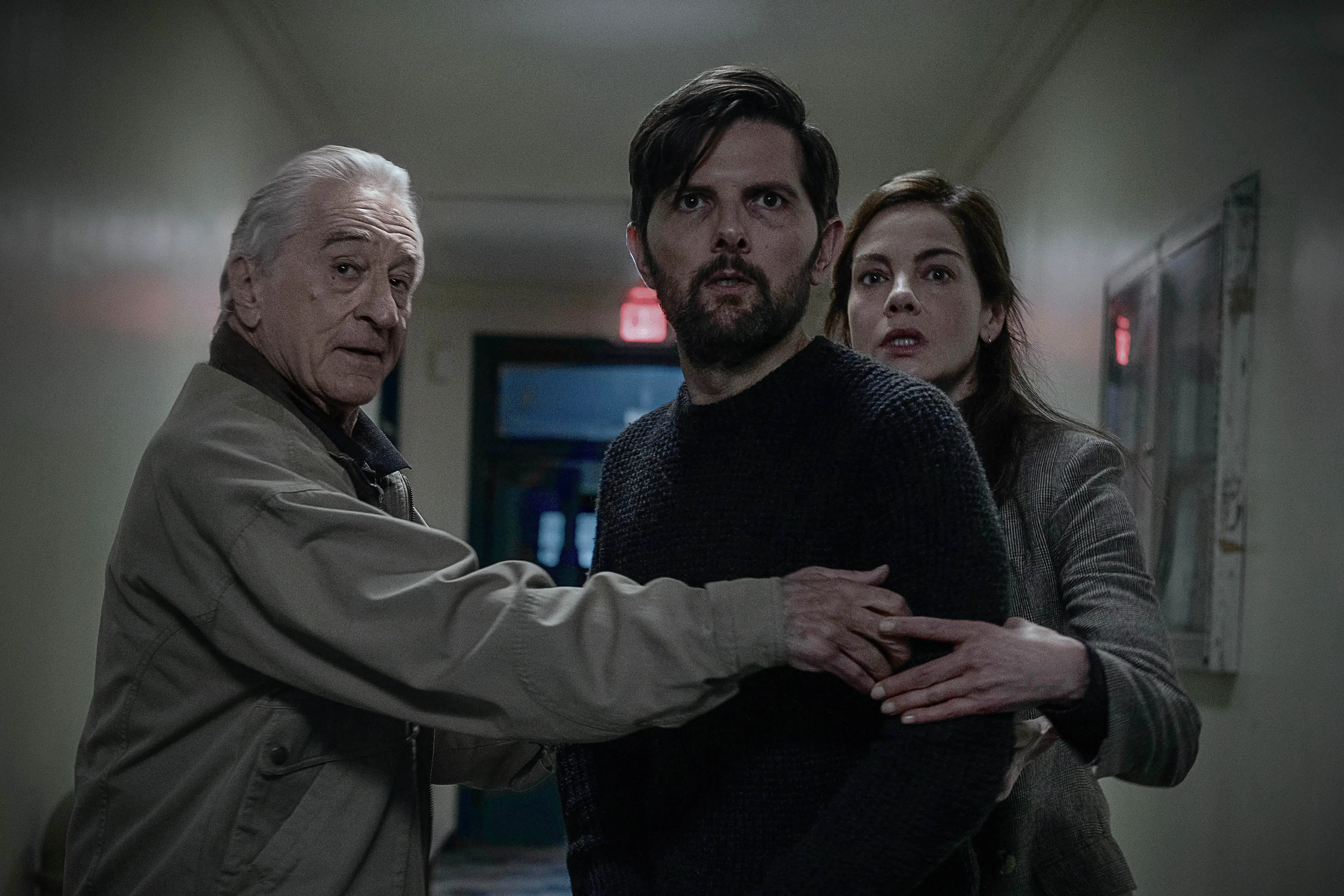 Robert De Niro and Michelle Monaham holding back Adam Scott in a hallway
