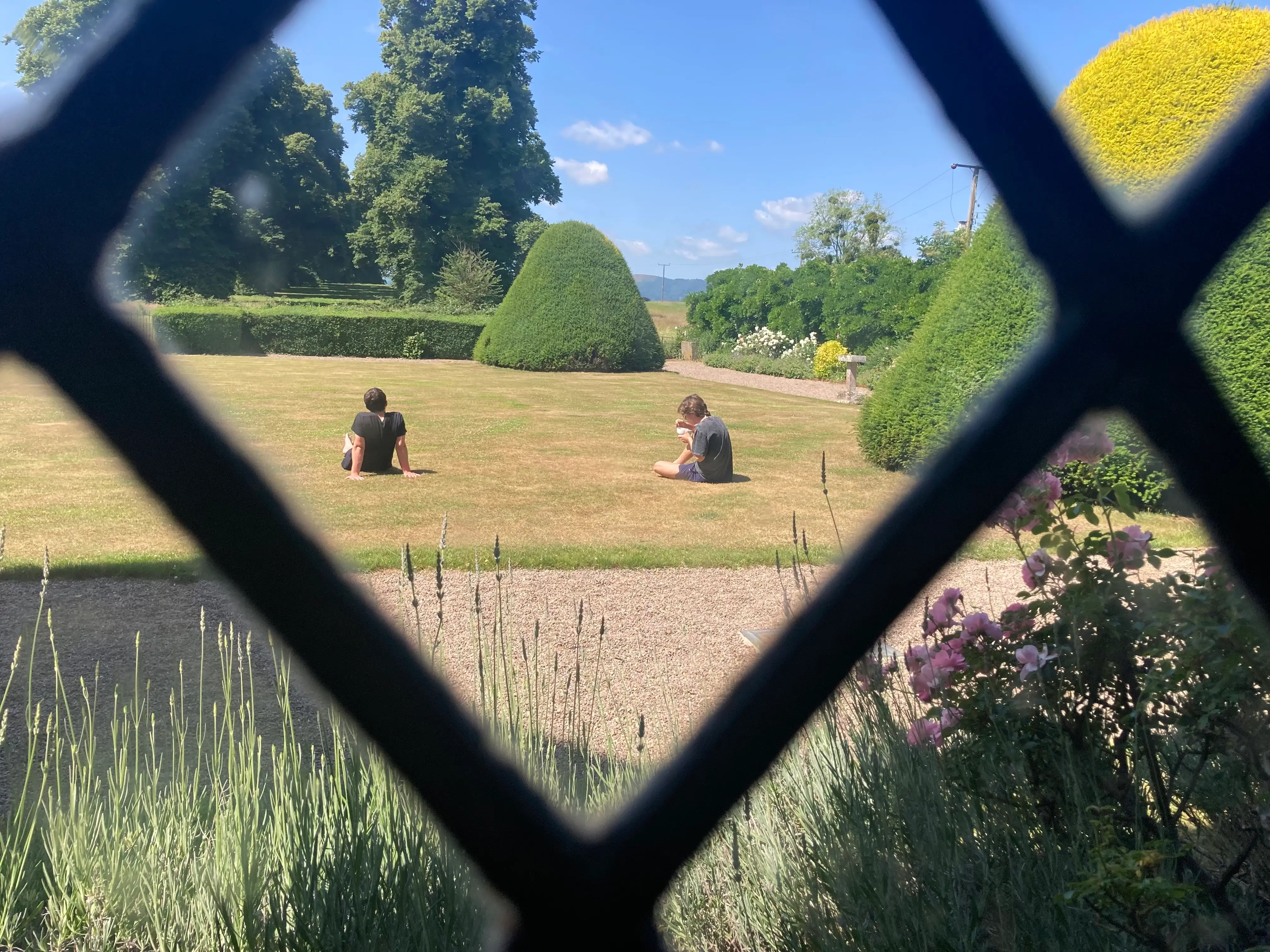 Two people relax on a lawn, as seen through leaded-glass windows.