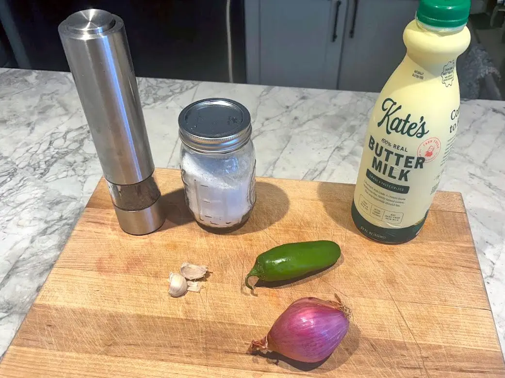 Salt, pepper, garlic, buttermilk, a jalapeño, and a shallot on a cutting board.