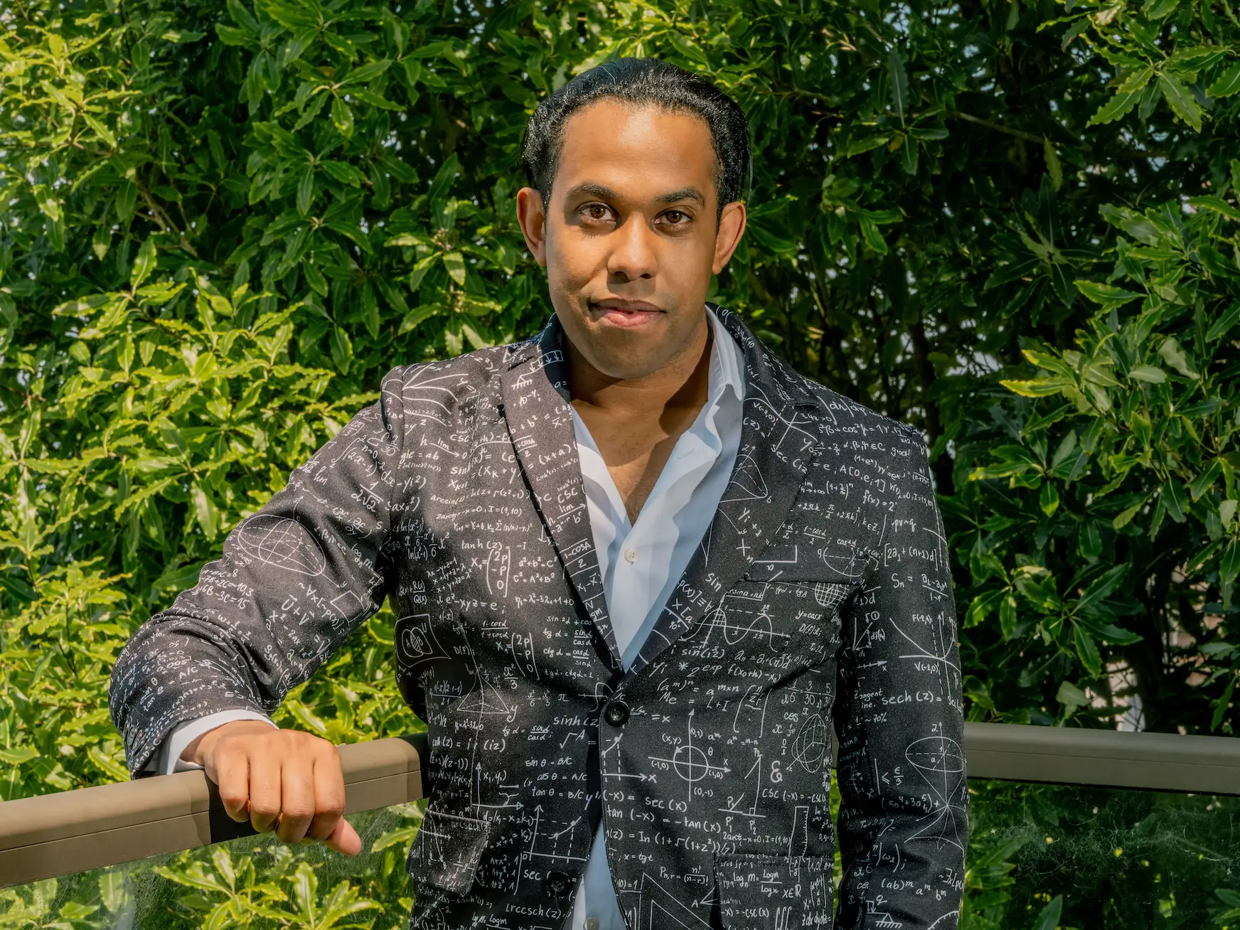 Infinity founder and CEO Jeremy Nixon, standing on a balcony in front of trees, wearing a sportcoat with math equations written on it.